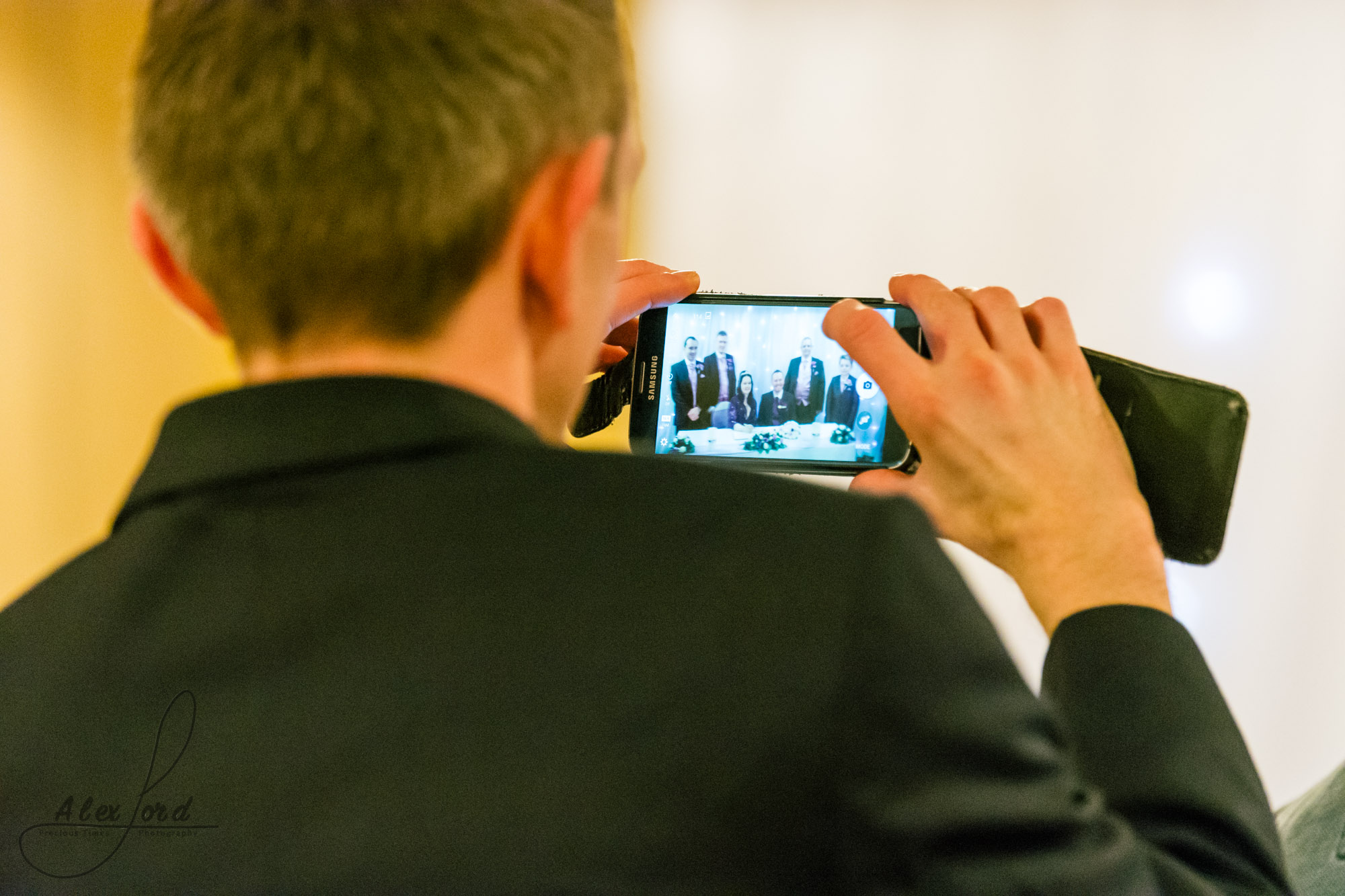 a wedding guest takes a photo of the signing of the register from his seat