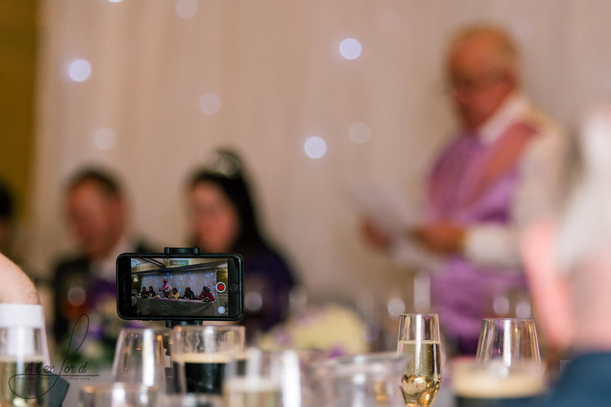 a wedding guest takes a photo of the brides father giving his speech