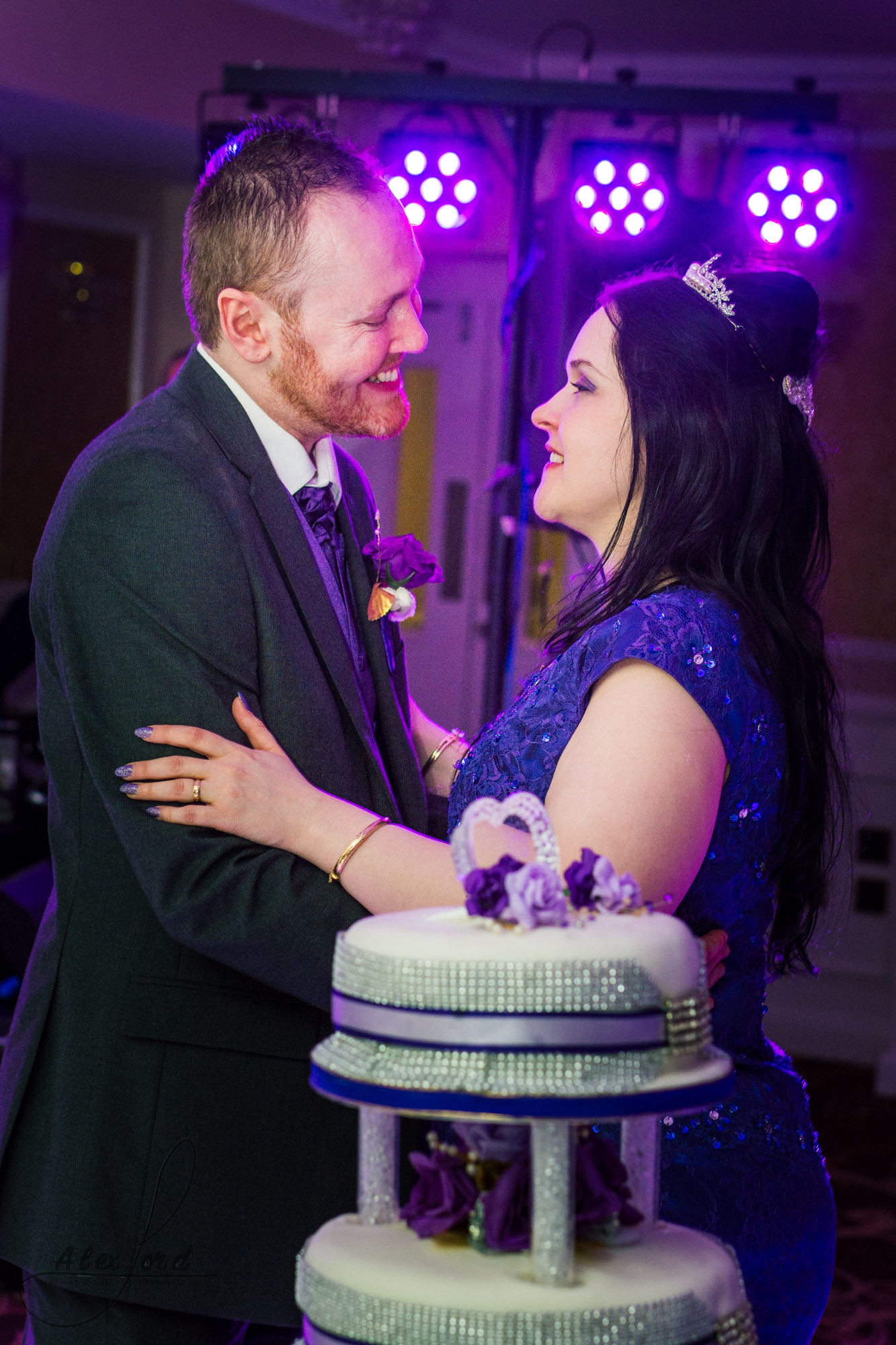 the bride and groom stand behind the wedding cake and pose for a photo