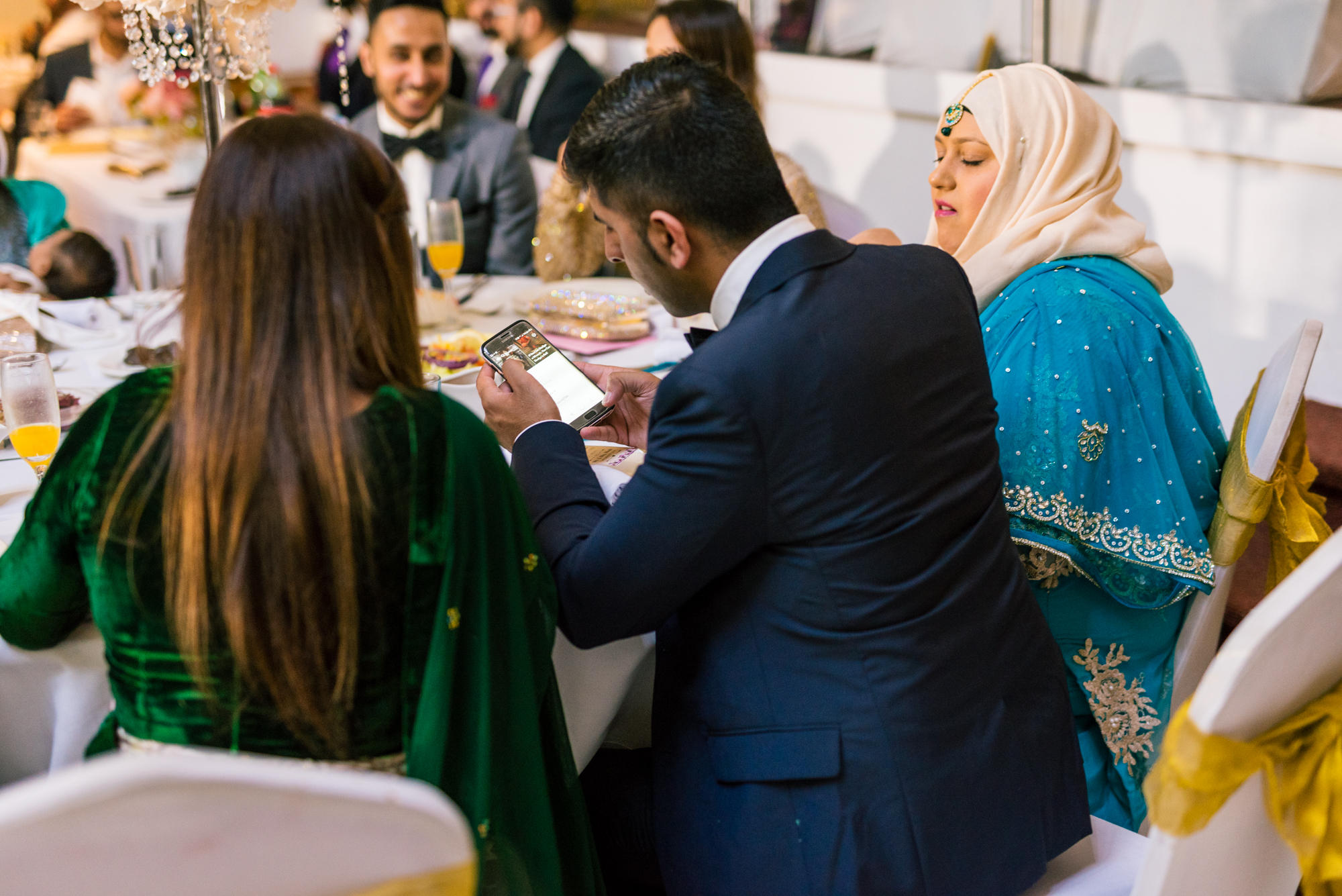 two guests at the wedding sit and look at their phone