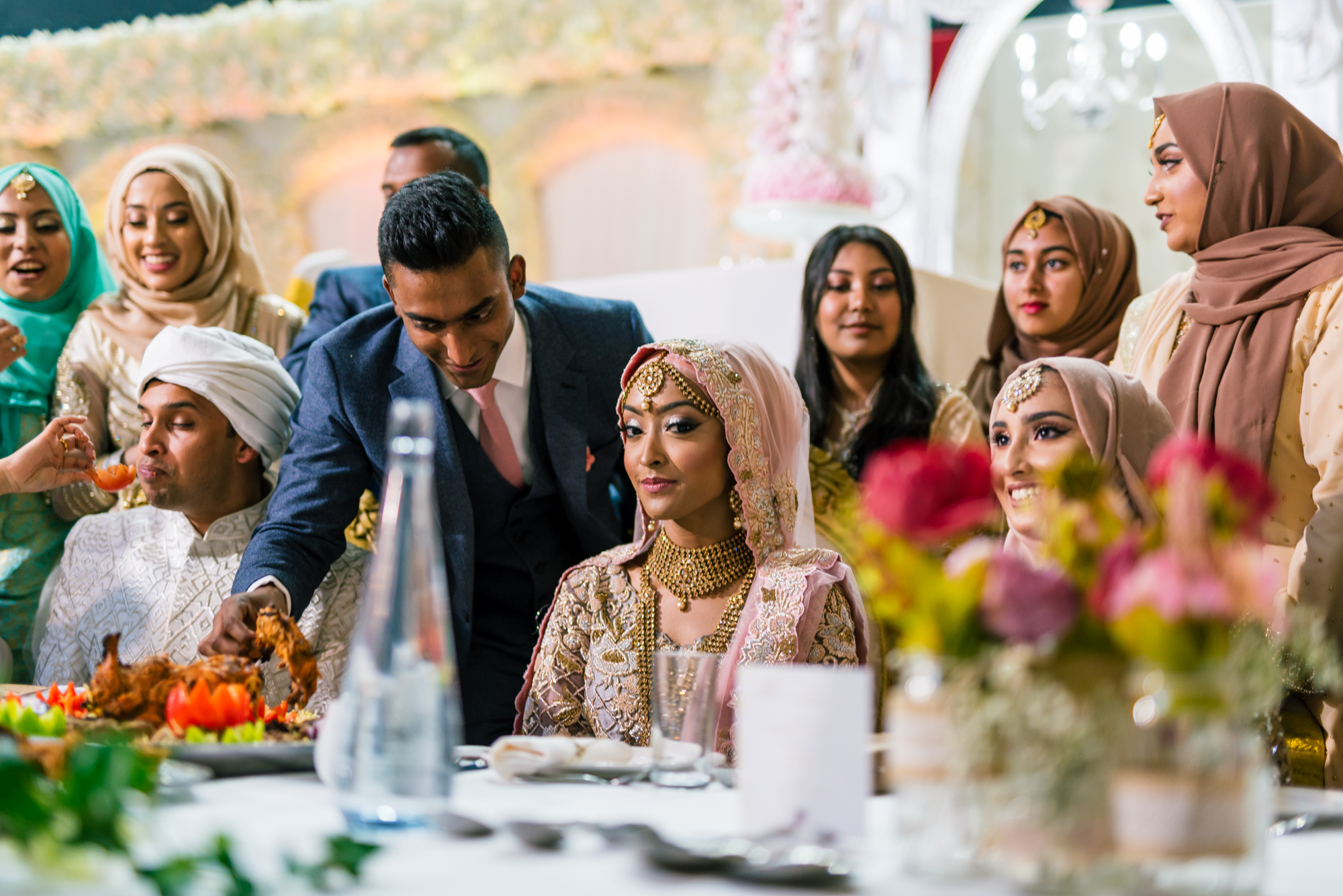 the bride and groom and their family gather round a large table full of indian wedding food