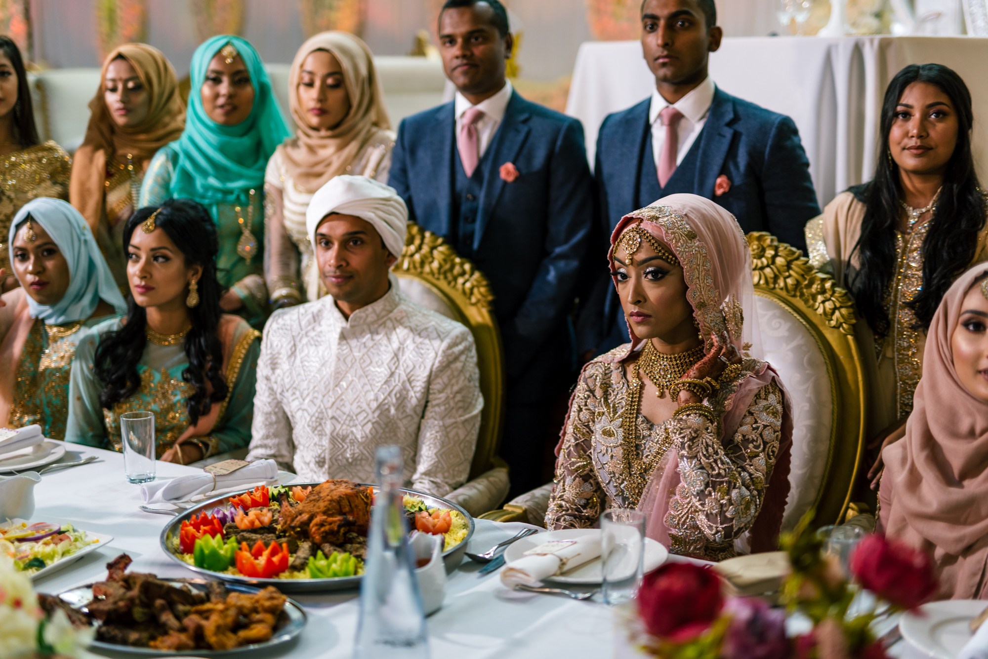 the bride and groom sit on their table with lots of indian food in front of them