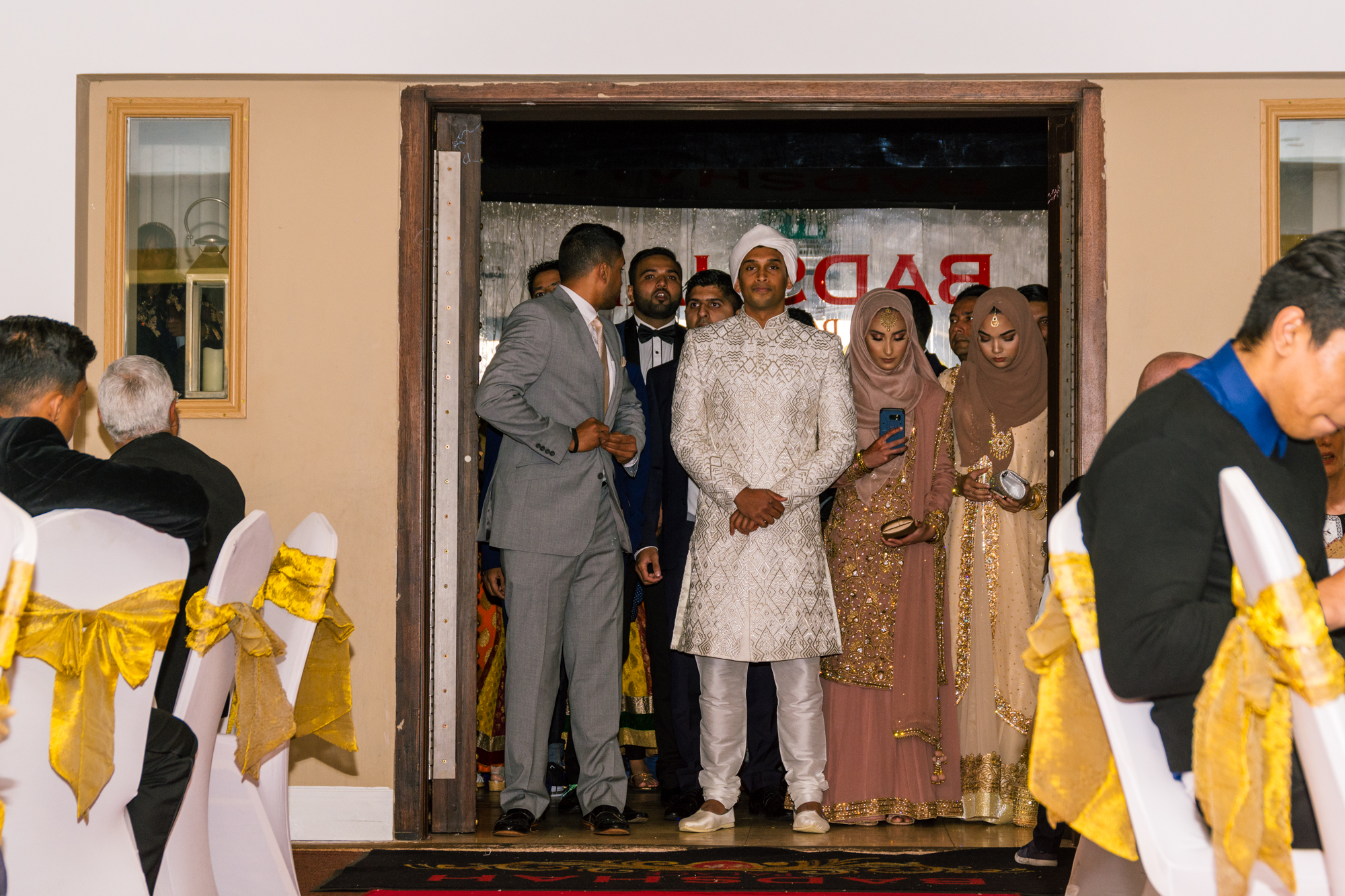 the bride and groom depart the wedding venue with their family behind them