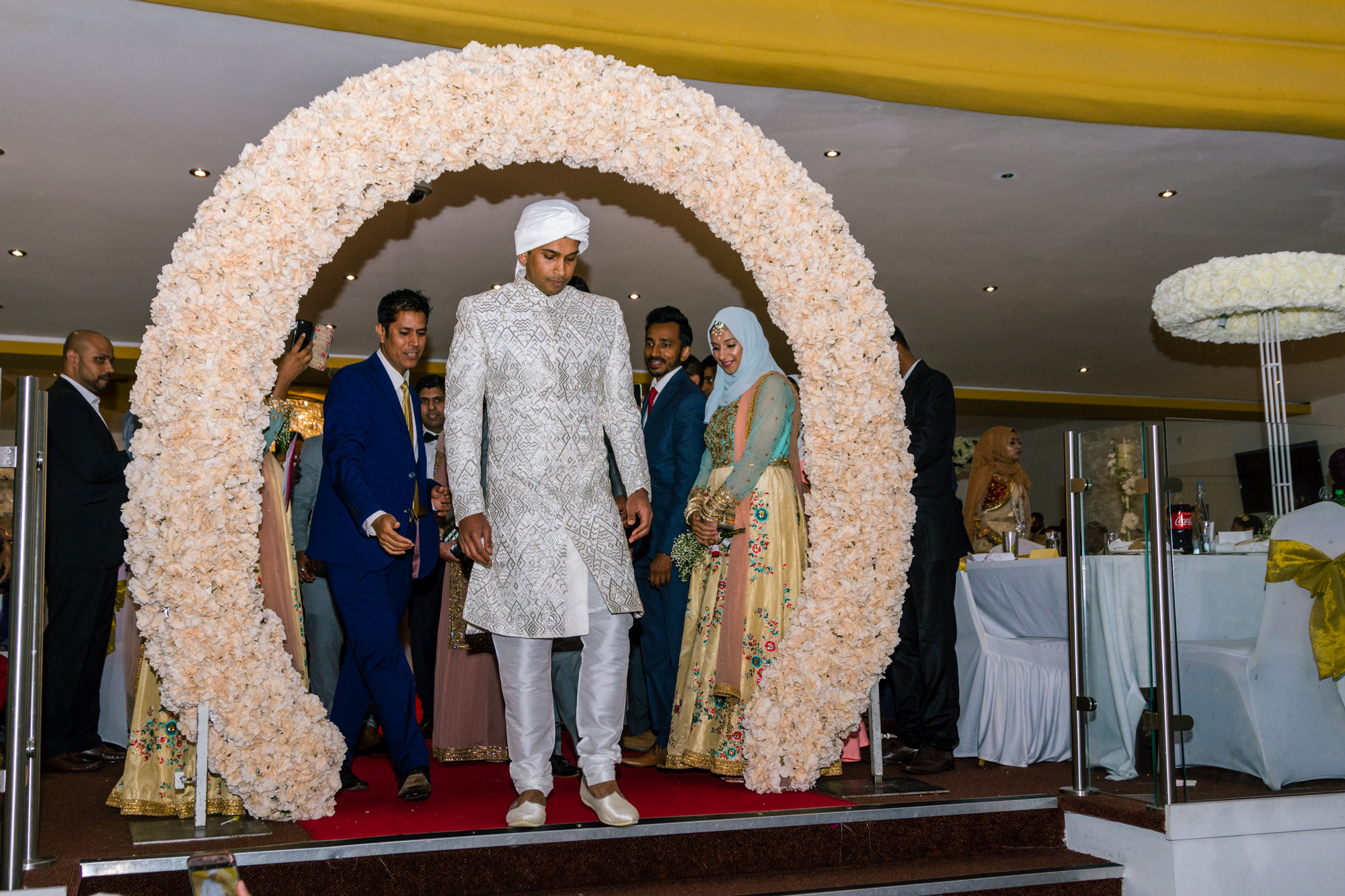 the bride and groom stand under a large floral arch before they leave the wedding venue