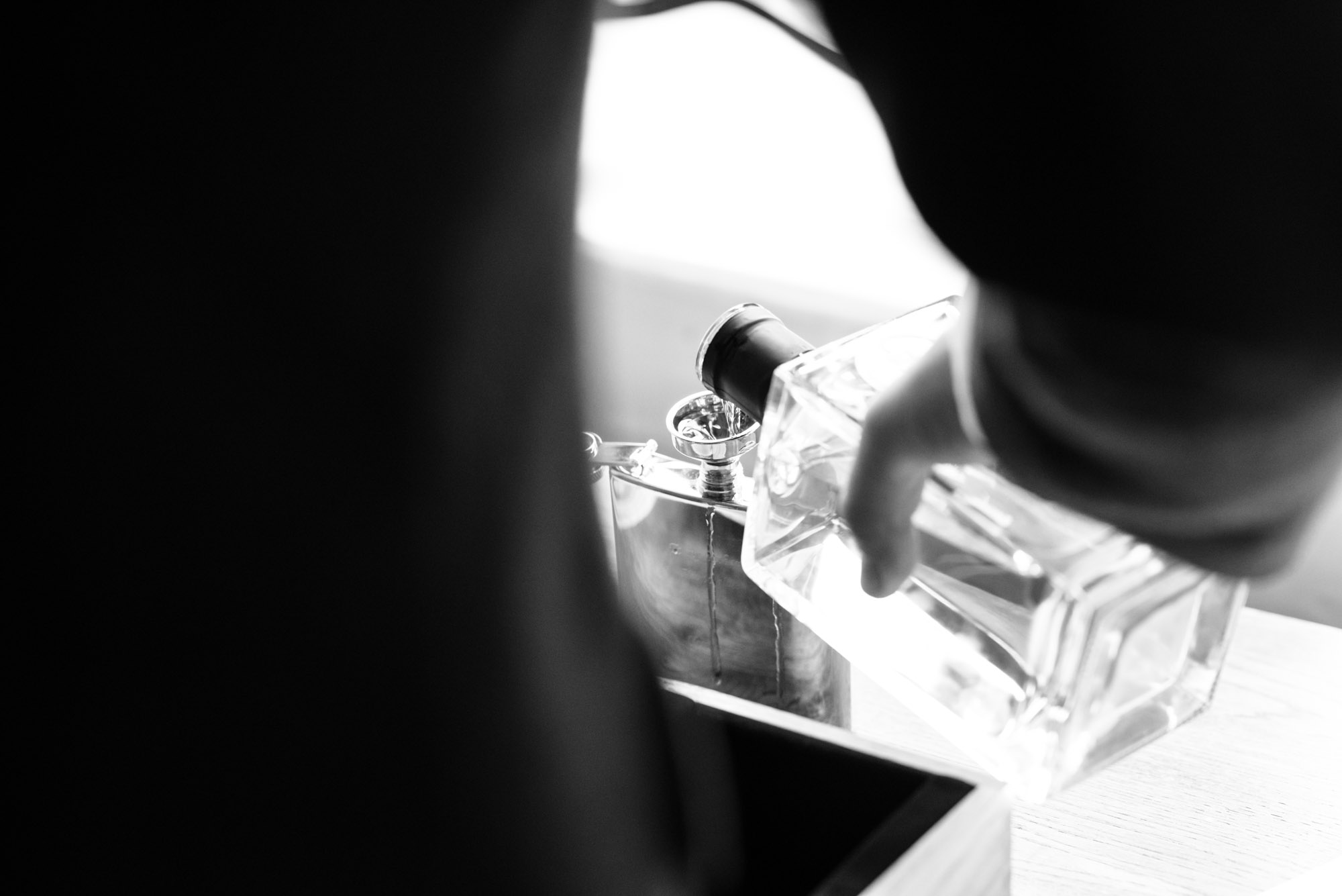 Daylight through the window lights whiskey being poured into a hip flask.