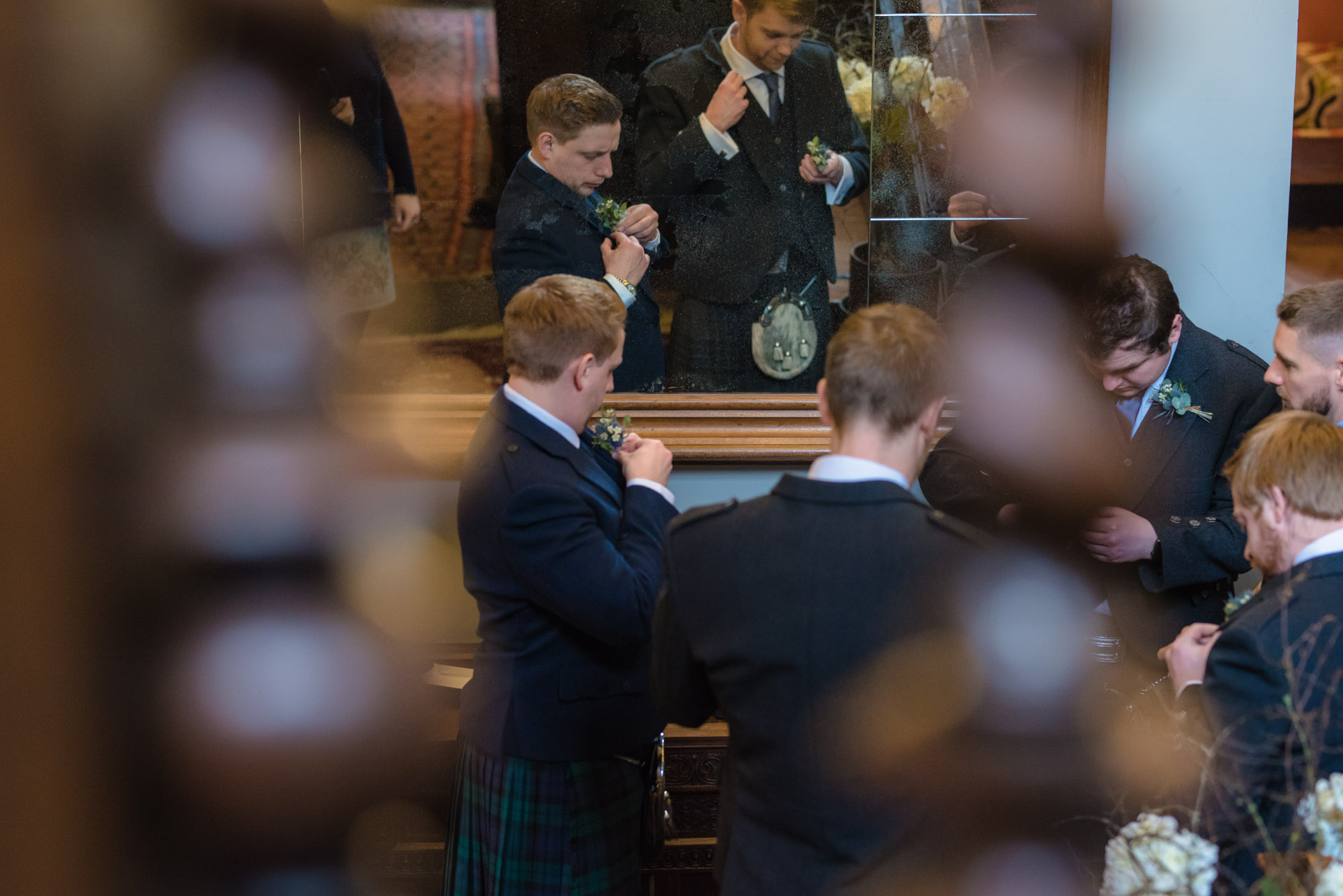Groom and his groomsmen stand together and put their flowers on their suits.