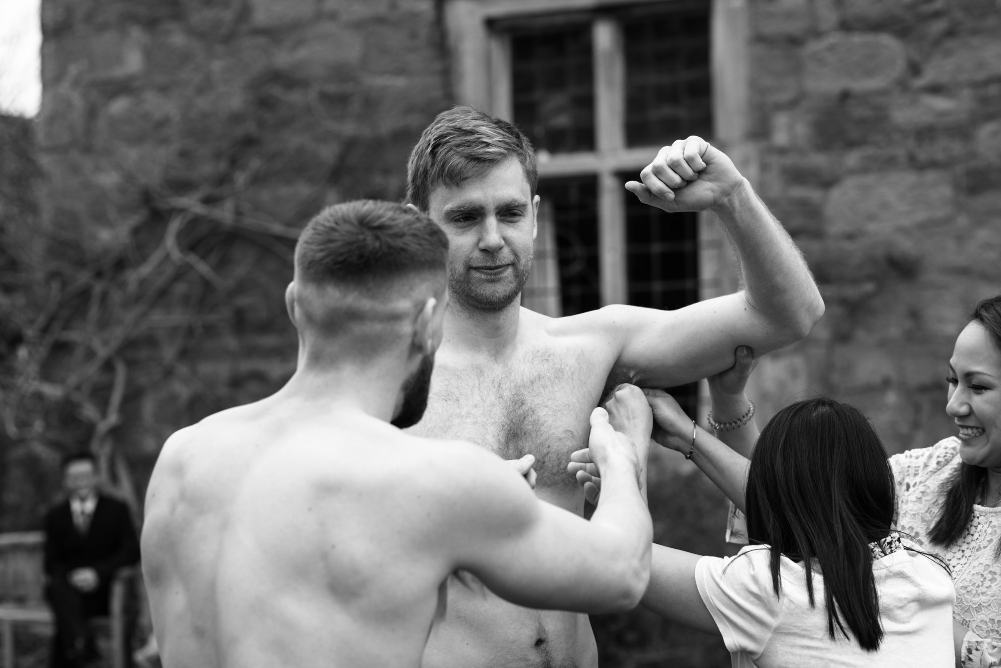 The best man with his top off has a wax strip applied under one of his arms.