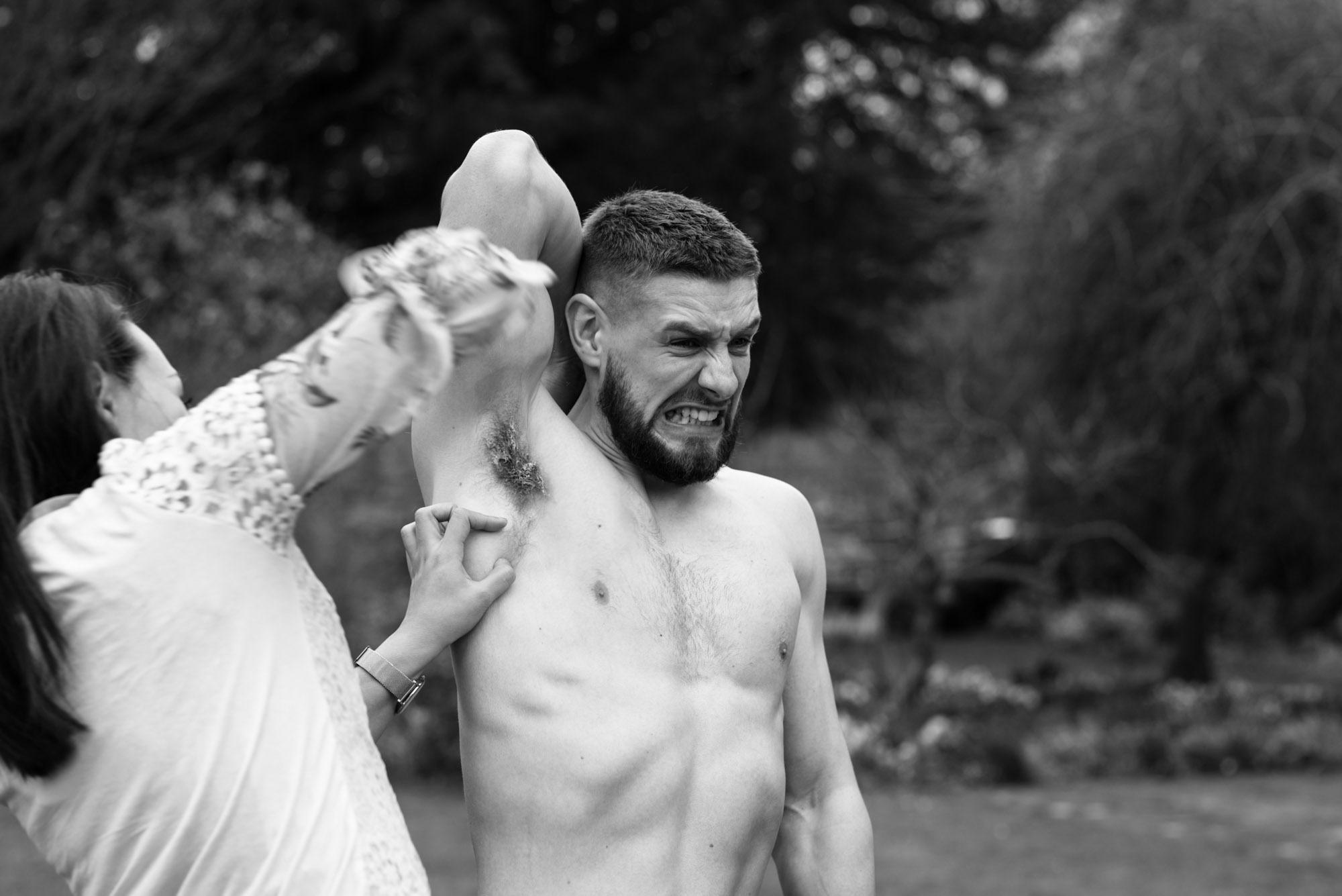 One of the wedding party pulls a wax strip from under the bet mans armpit.