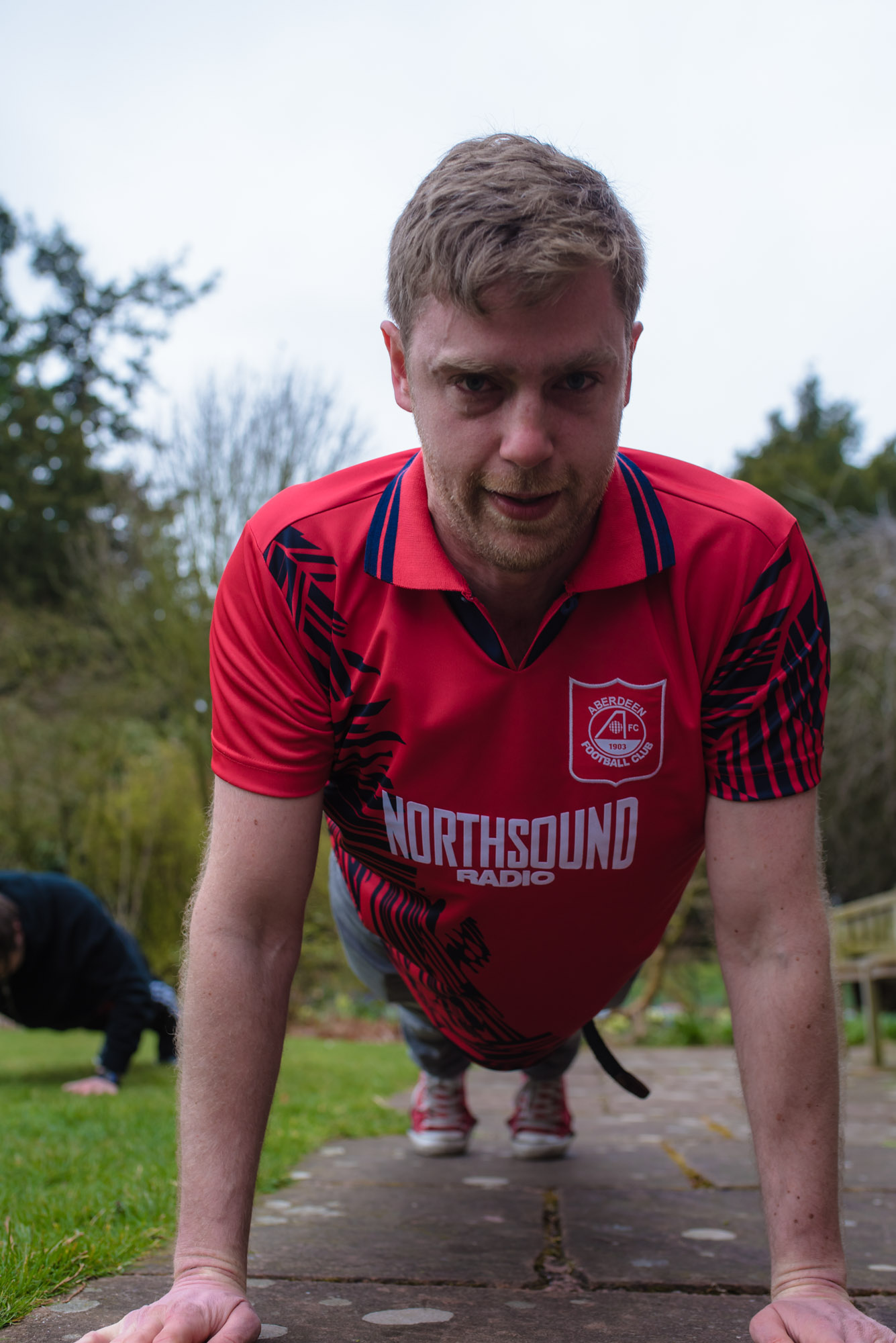 Member of the wedding party wearing a red top crouches down to do a press-up