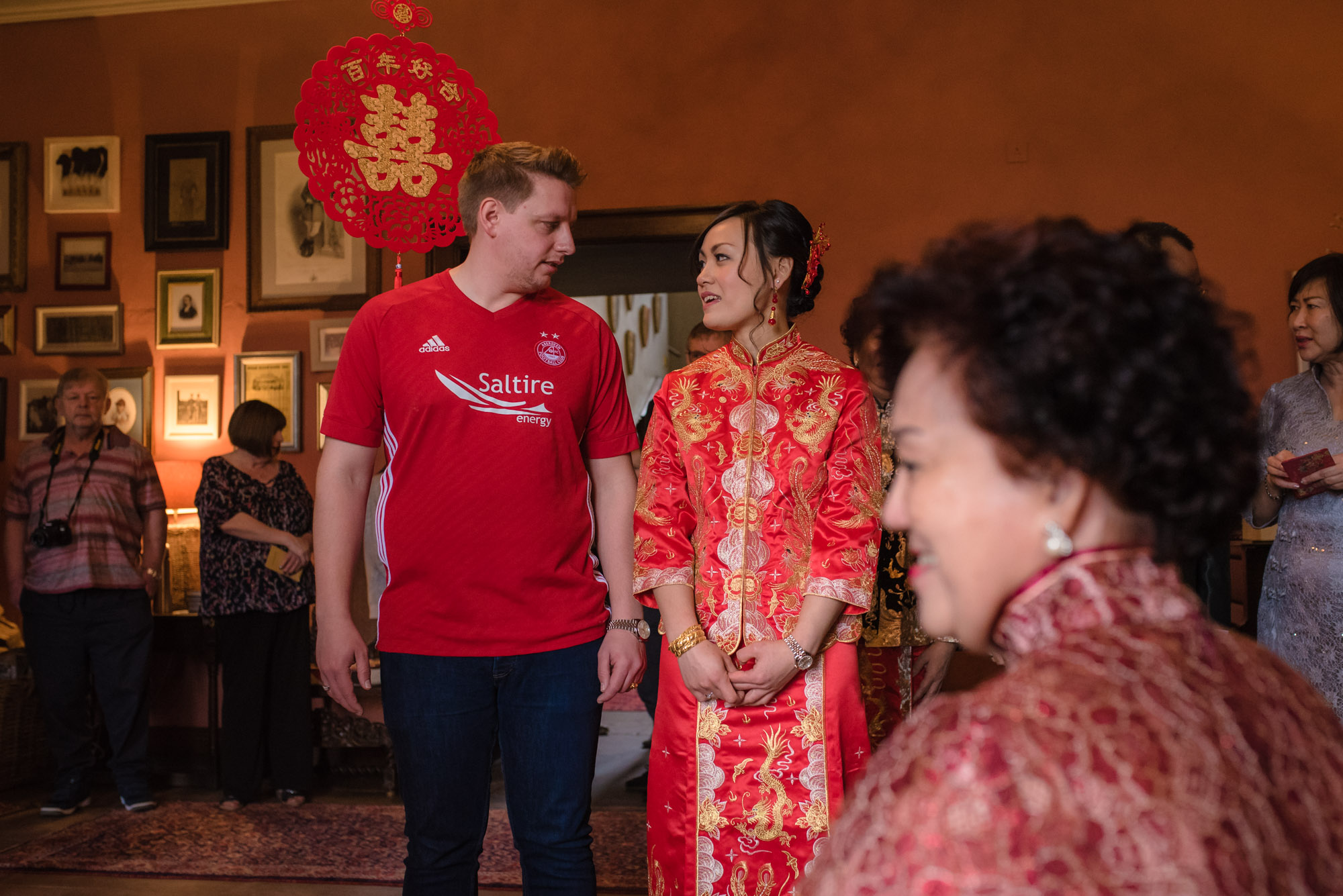 The bride and groom dressed in red stand and wait for the Chinese tea ceremony.