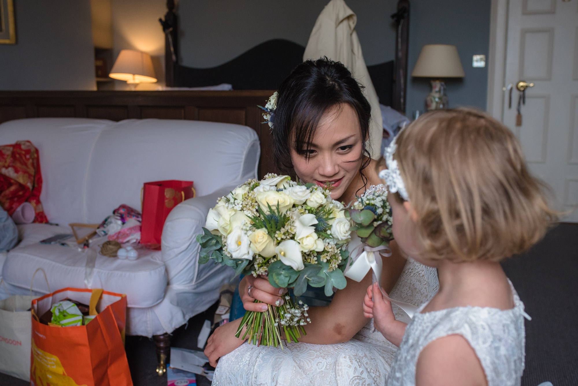 The bride kneels down to show the flower girl her bouquet.