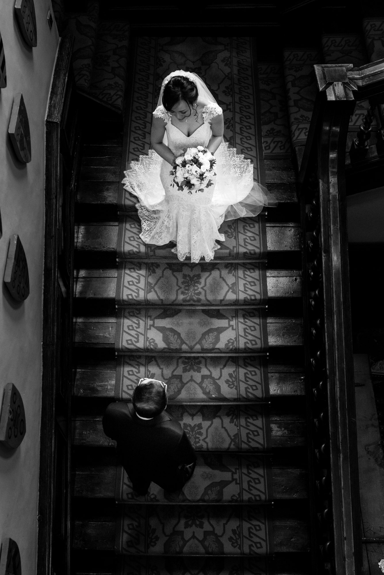 The bride, lit up by the sunlight, stands just behind her father on the stairs of Askham Hall.