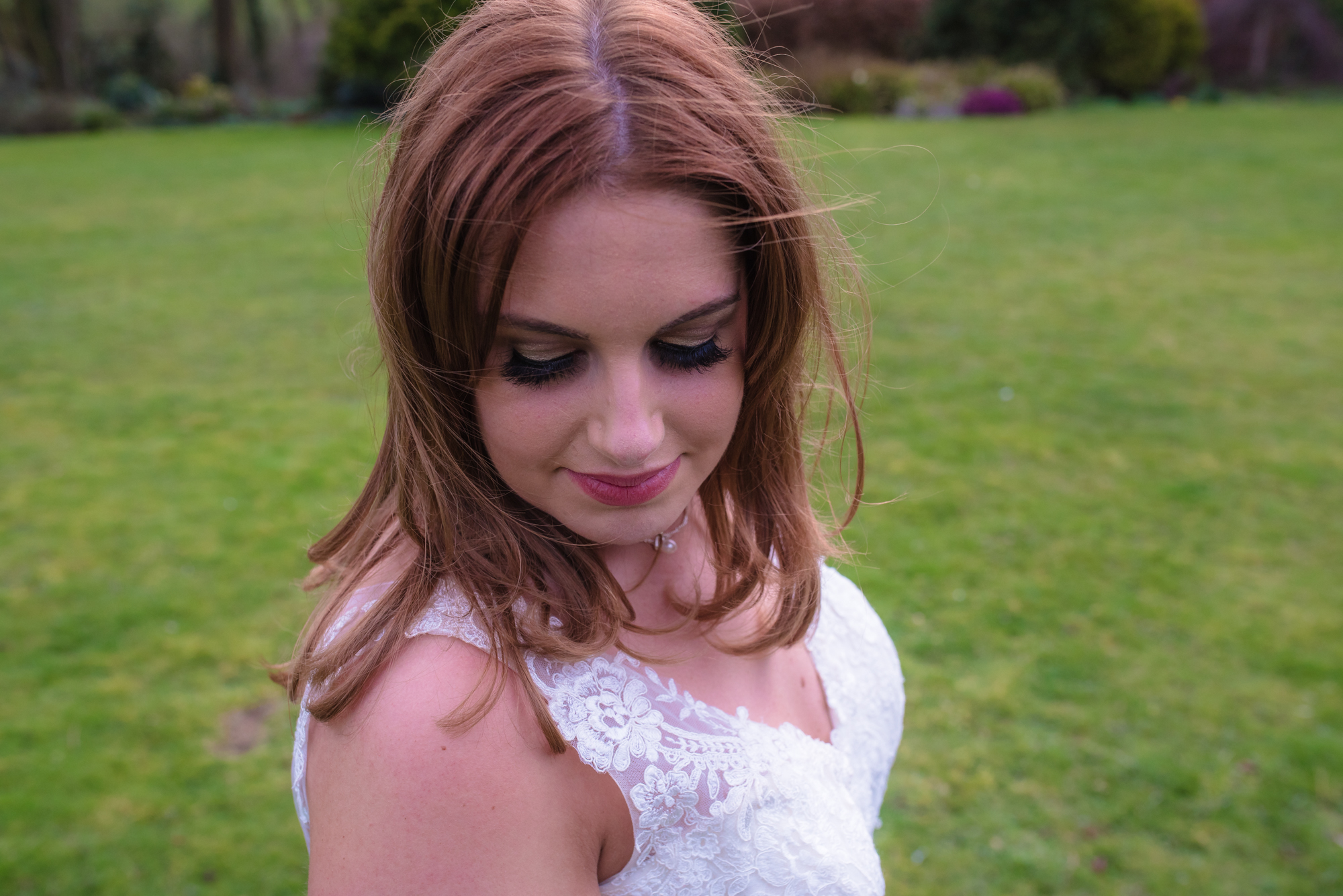 The bride looks towards the ground as she stands and poses for a wedding photo.