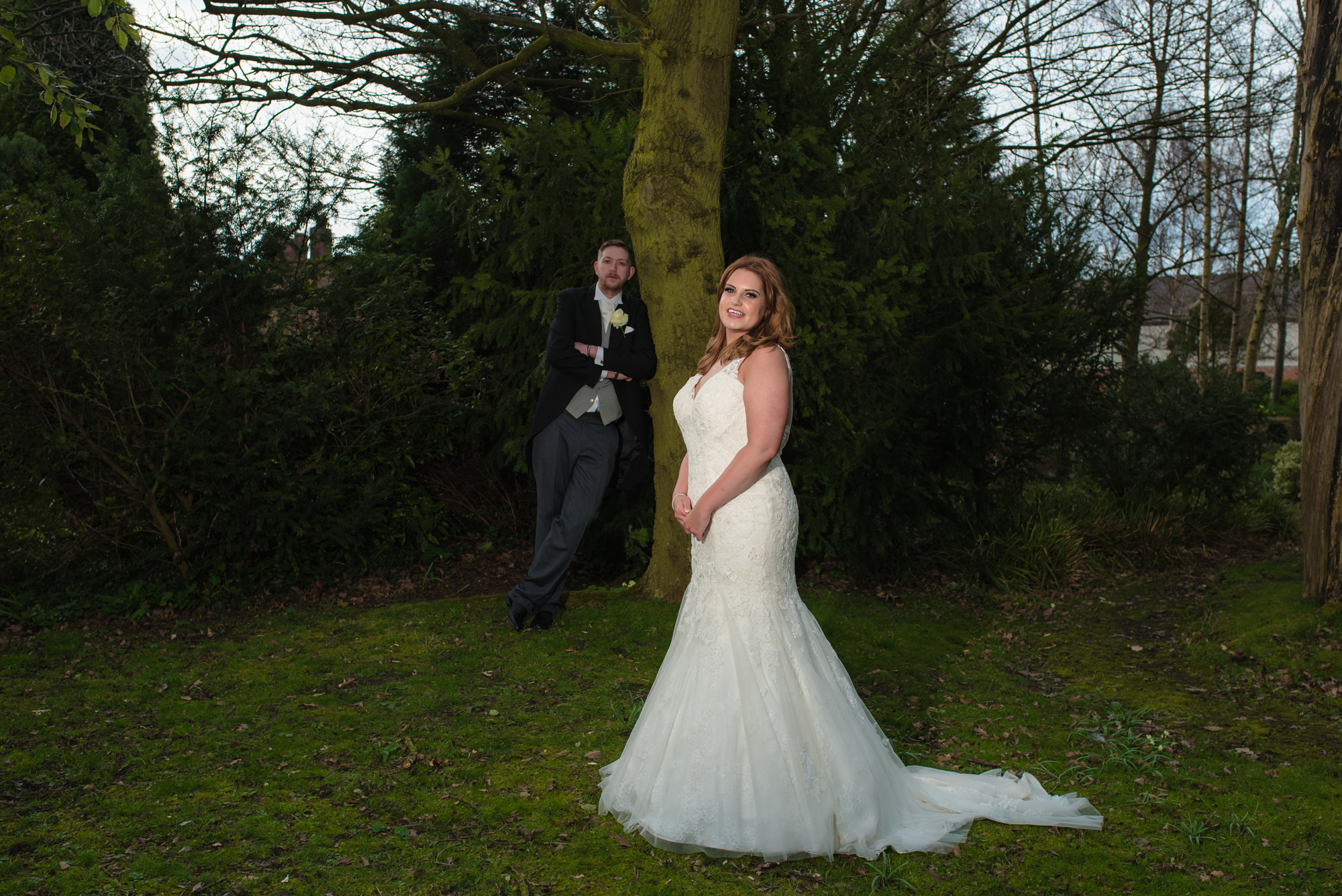 The bride and groom stand by a tree in the grounds of crabwall manor.