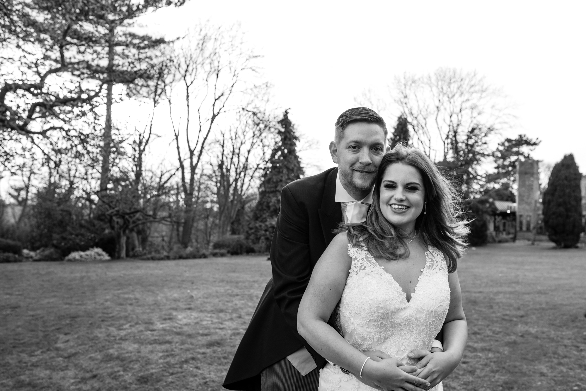 The groom stands and hugs his new bride in the grounds of crabwall manor.