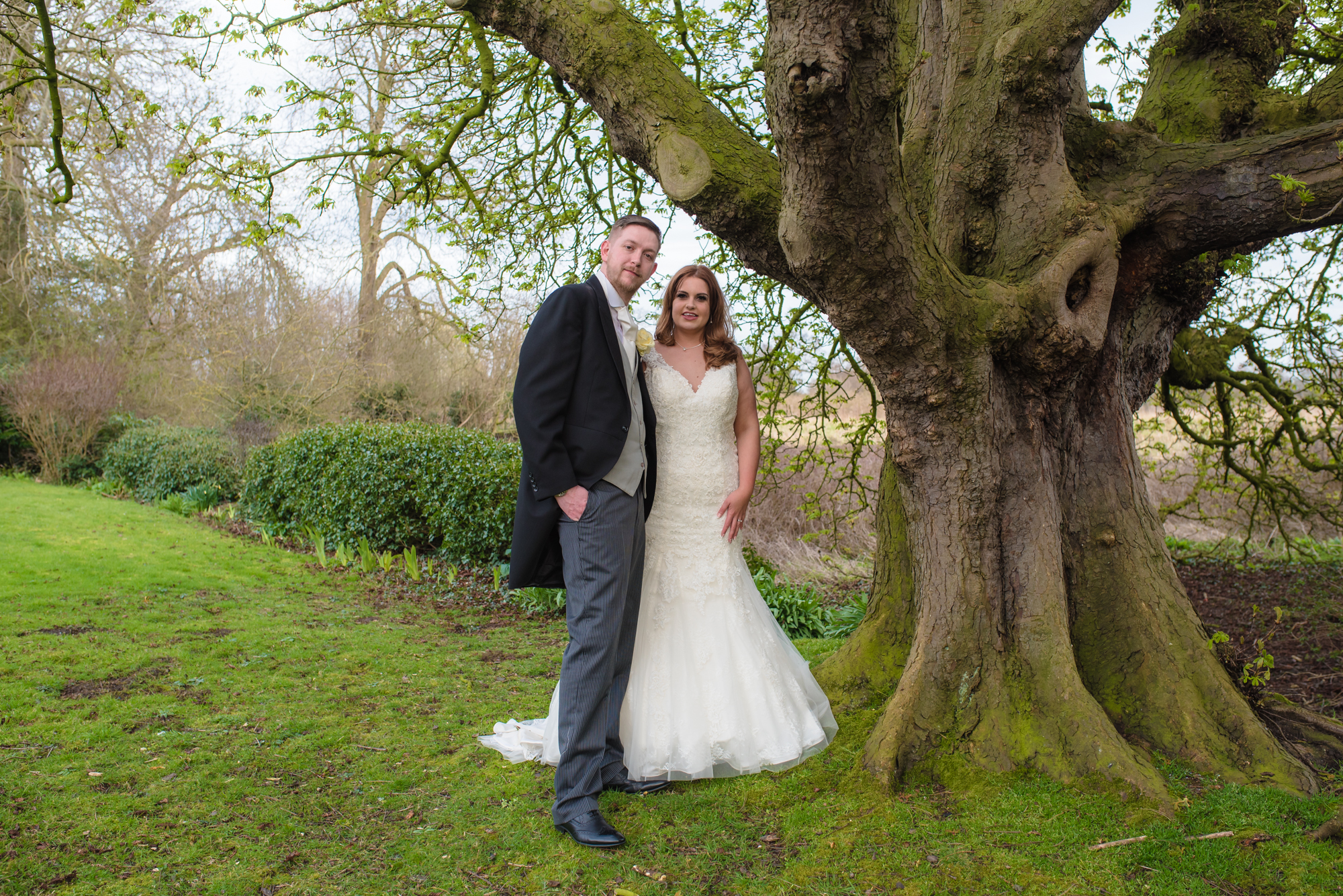 Bride and groom stand under a tree at crabwall manor.