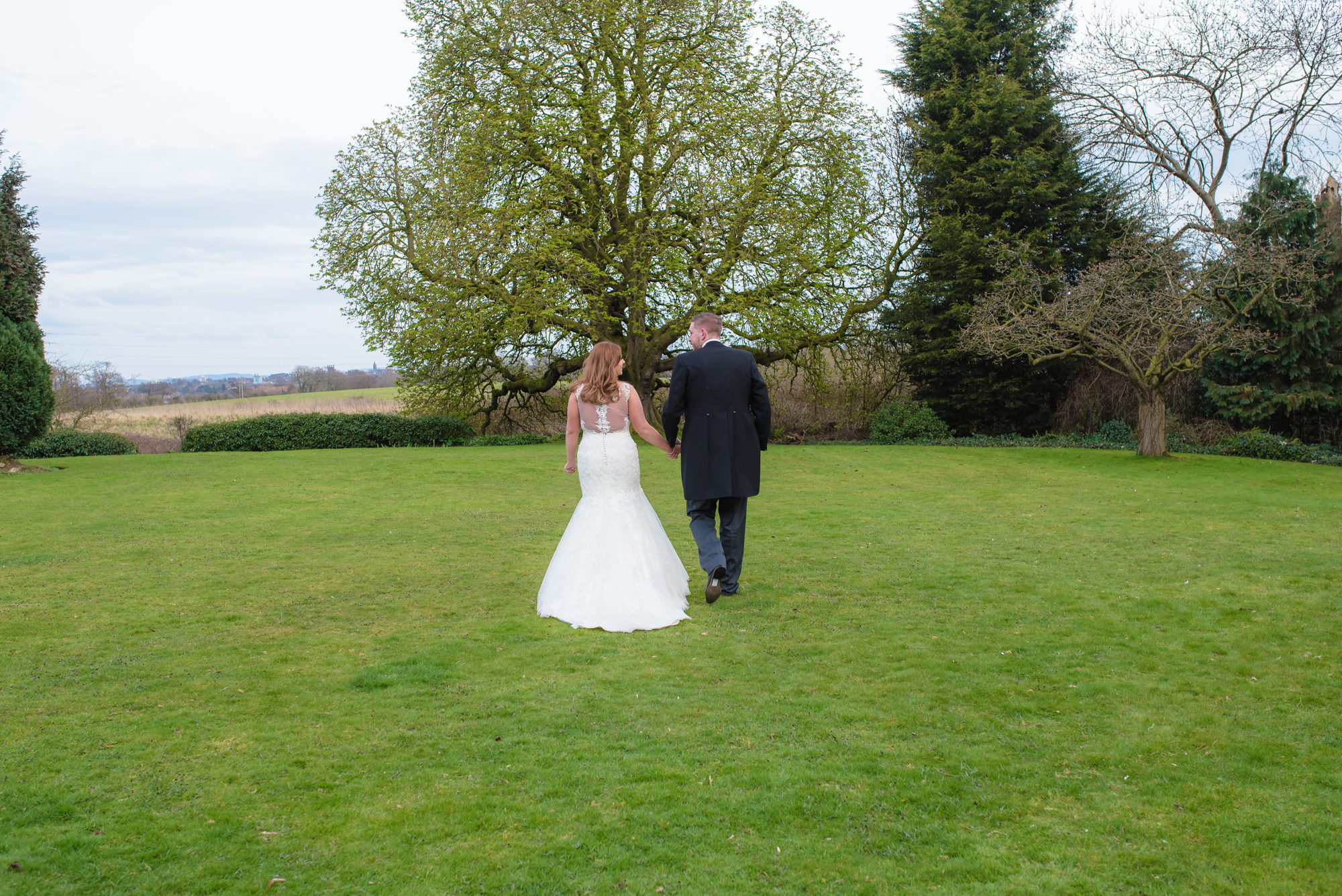 The bride and groom walking away from their wedding venue towards fields in the distance.