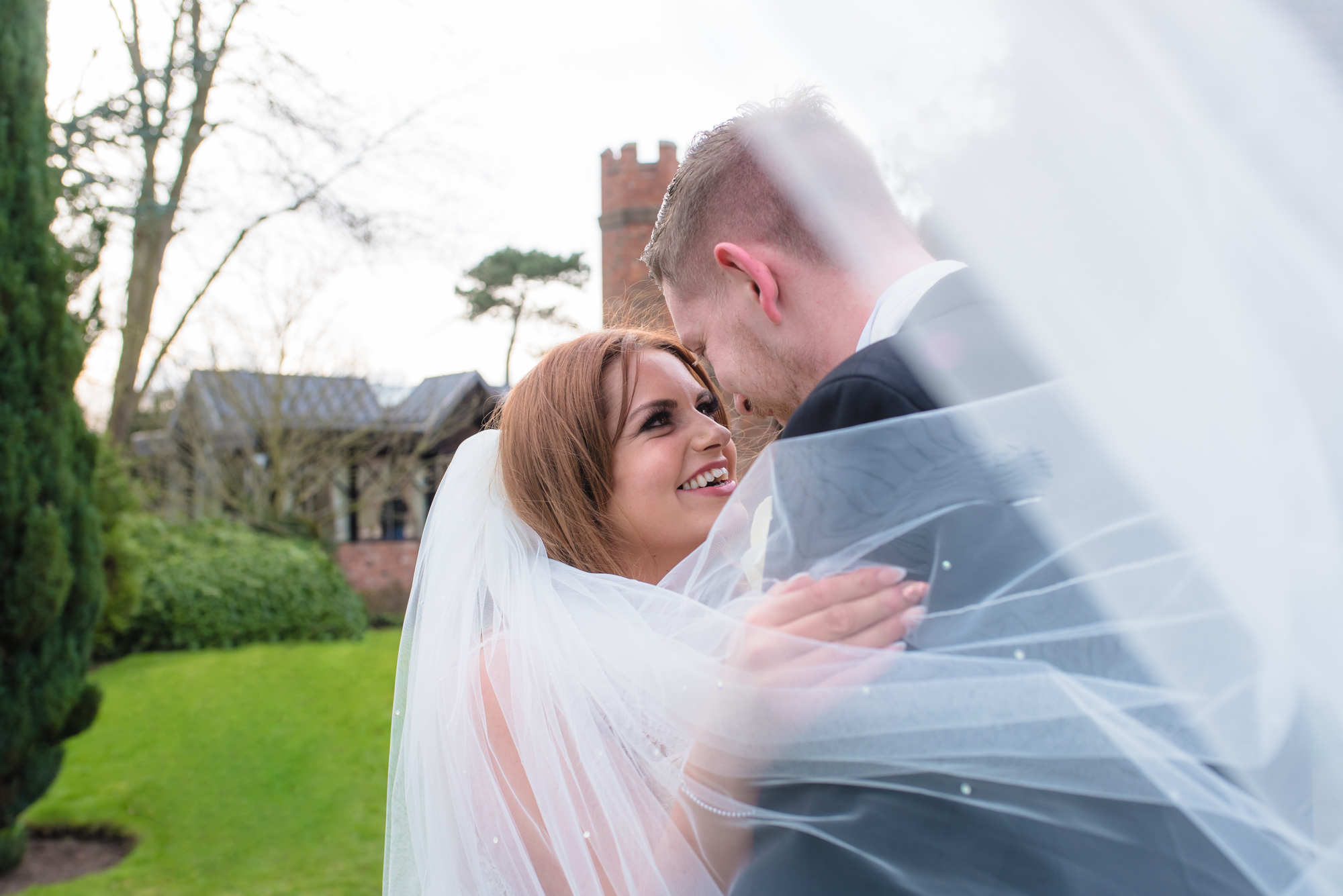 The brides veil partially covers her face as she smiles to her husband.