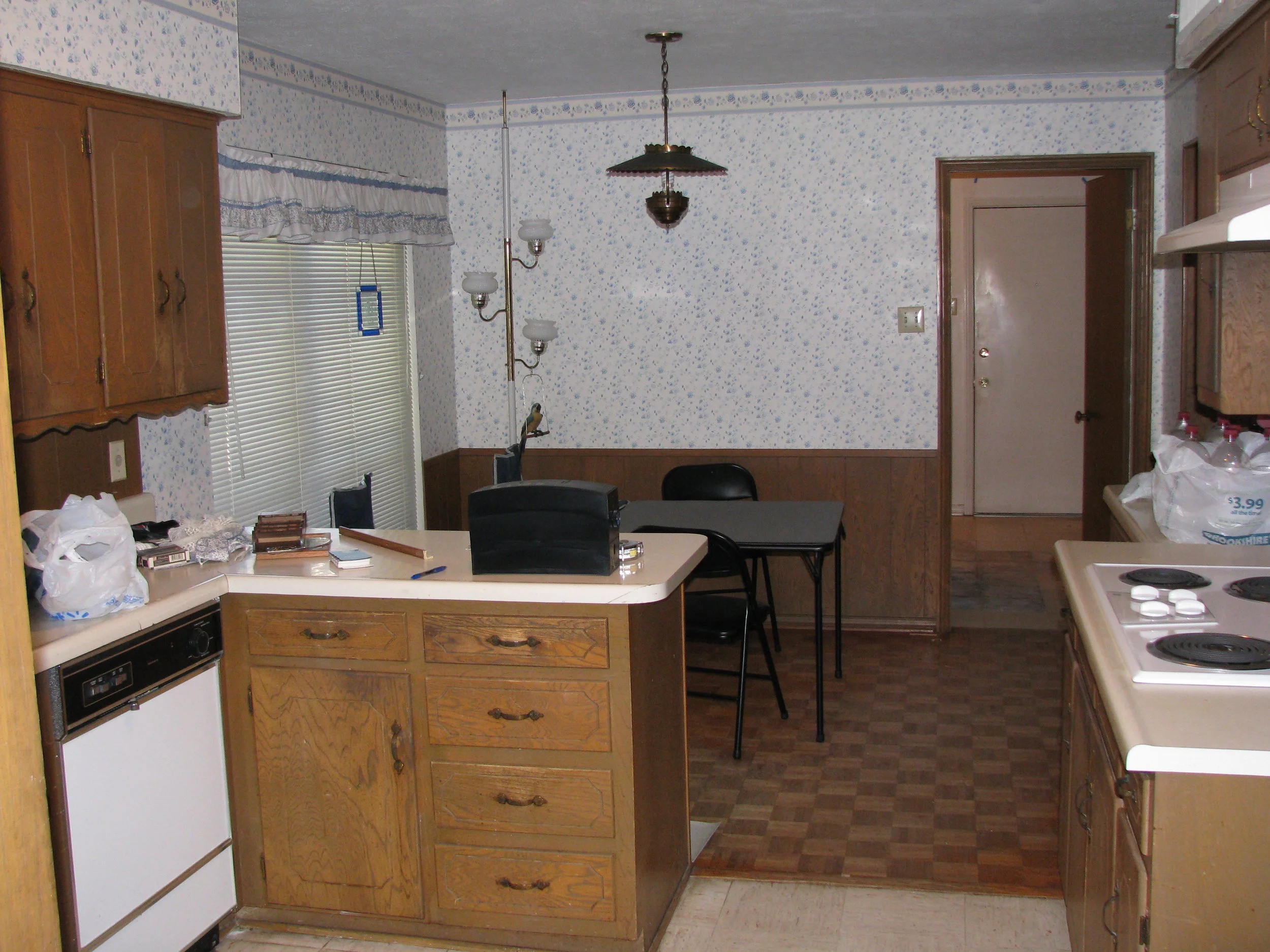 Kitchen before with worn cabinets, dated formica counters and 2 floor types