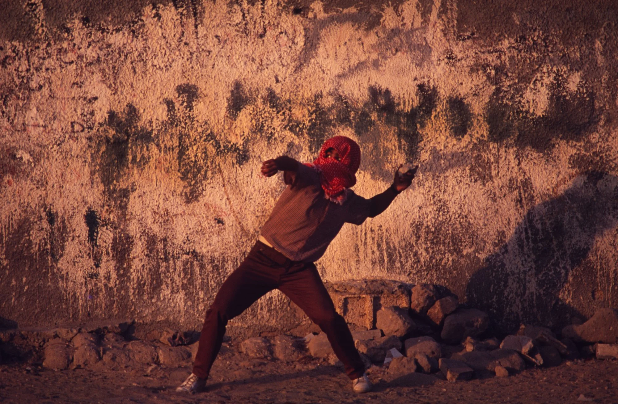 A member of the PLO hurls a rock (during the First Intifada) at Israeli Army soldiers in the Gaza Strip. 1992