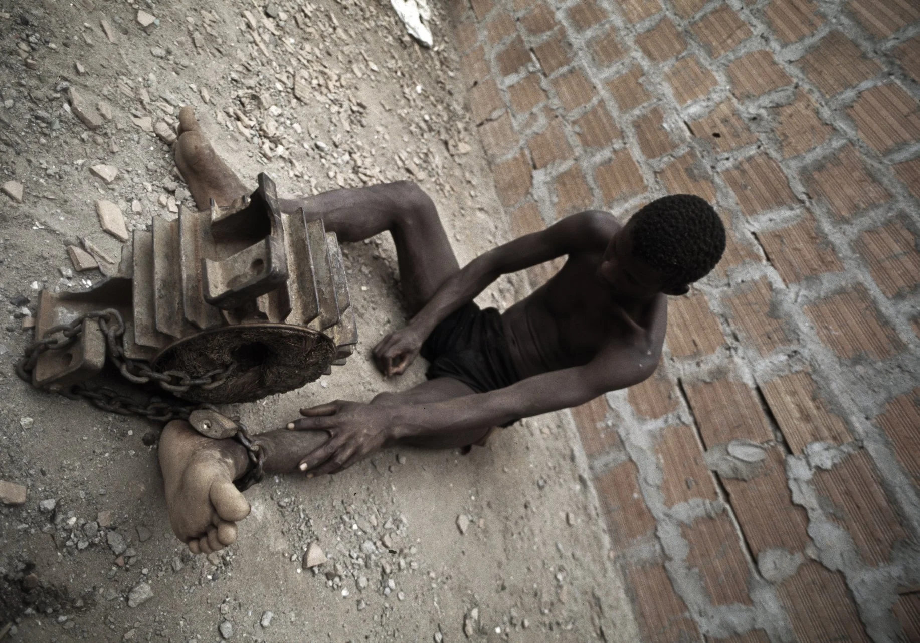 A former combatant of Angola's long running civil war is chained to an engine part at Papa Kitoko's mental asylum, Luanda, Angola, 1993
