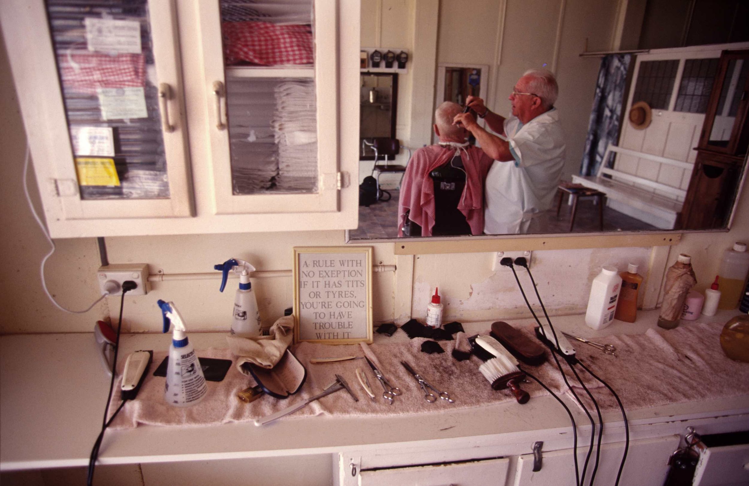  Barber. Outback Queensland. Late 1980s Note: Photographer doesn't condone sentiments in picture frame. 