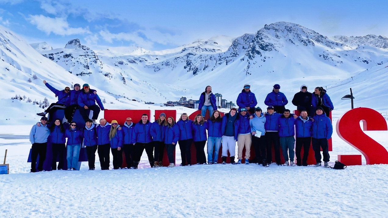 group of chalet hosts in uniform in front of the Tignes sign with the mountains in the background