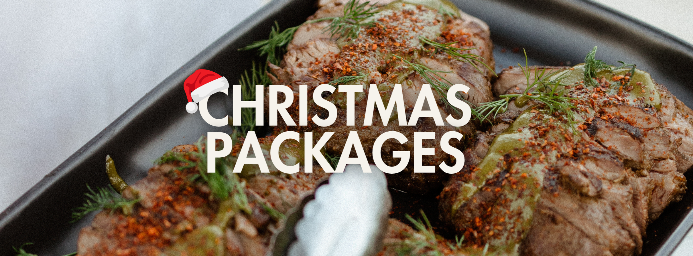 Close-up of cooked meat garnished with herbs and spices on a black tray, with a festive Christmas design and text overlay reading "Christmas Packages."
