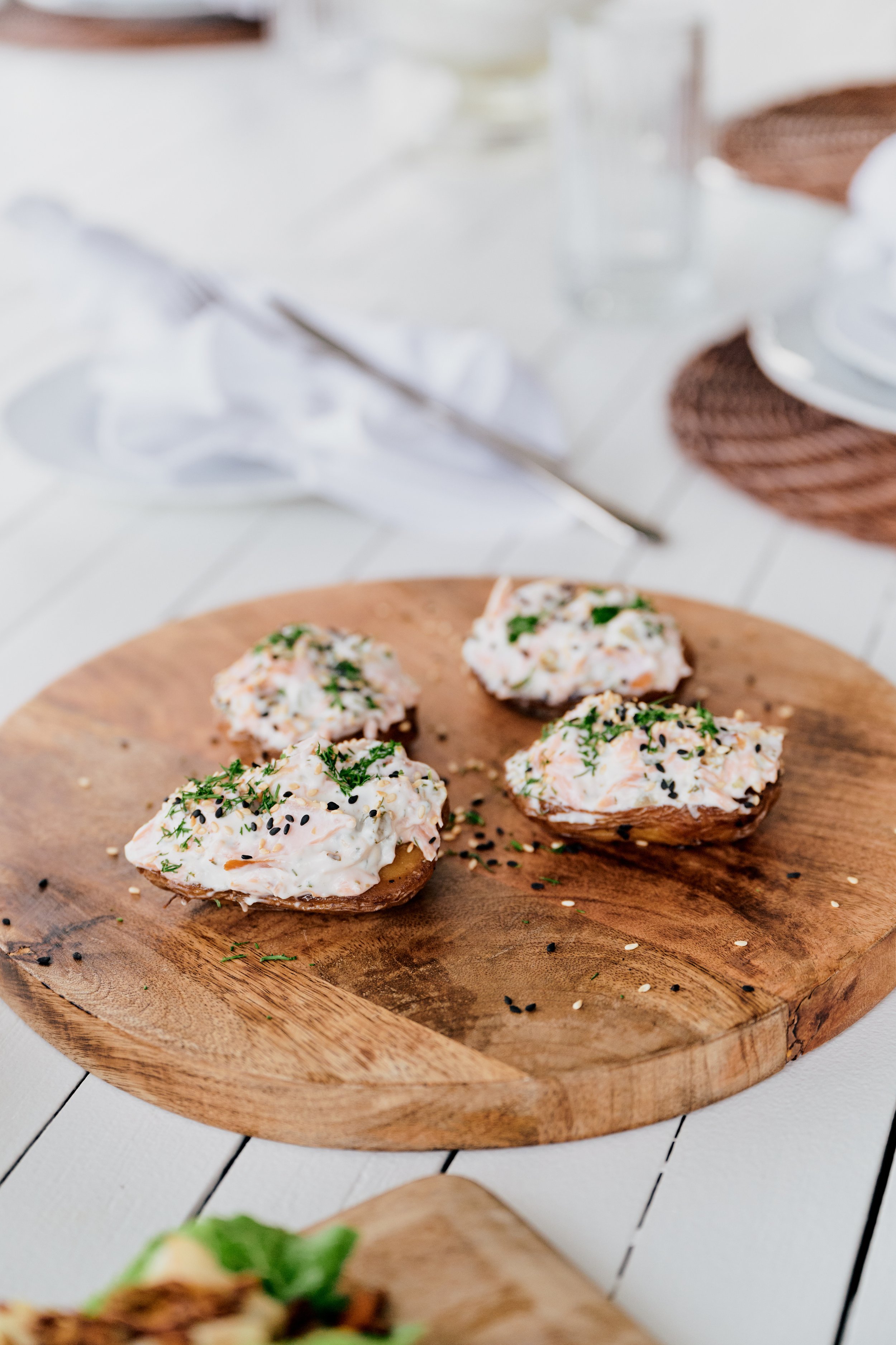 Snacks with a spread of creamy dipping sauce, garnished with herbs and sesame seeds on a wooden board.
