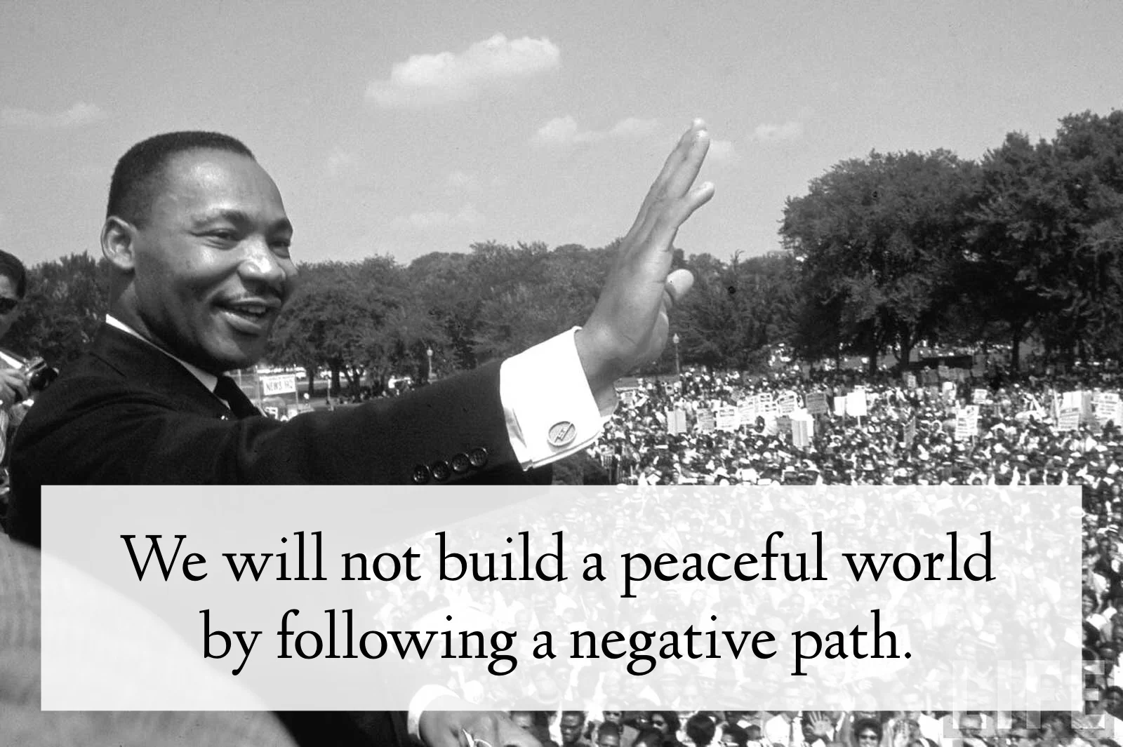 Image of Dr. King smiling and waving, in front of a huge crowd. The quote says "We will not build a peaceful world by following a negative path."