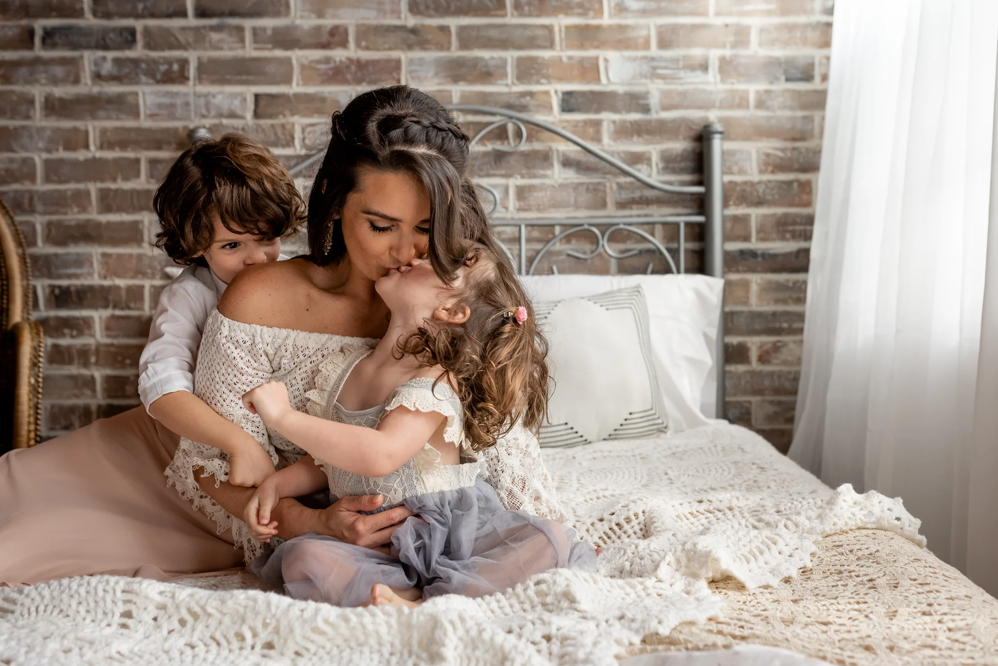 Beautiful mom and her baby girl in a natural light, boho studio with a brick wall, textures accents, peacock chair, and neutral details.