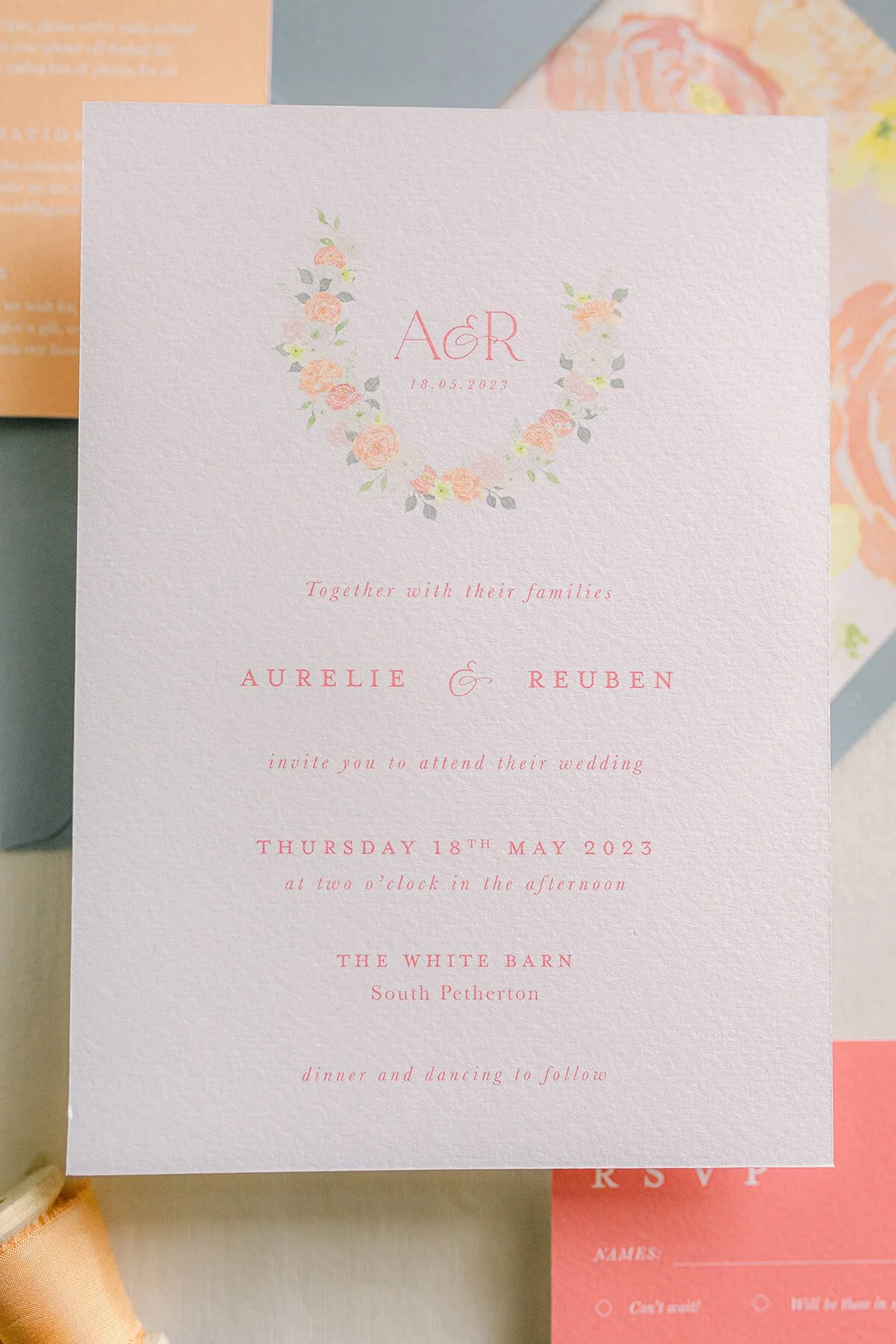 close up of wedding invitation with watercolour floral wreath with coral, peach, pink and yellow flowers.