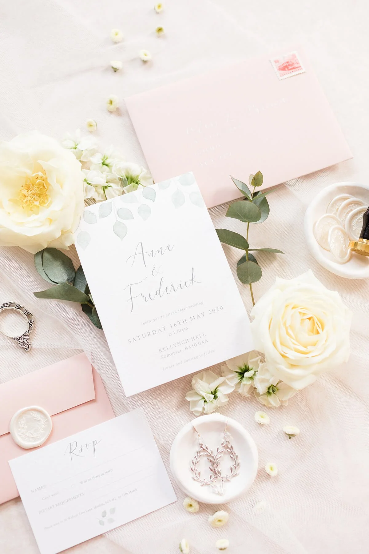 Wedding stationery flat lay with watercolour eucalyptus design, modern calligraphy and blush envelopes