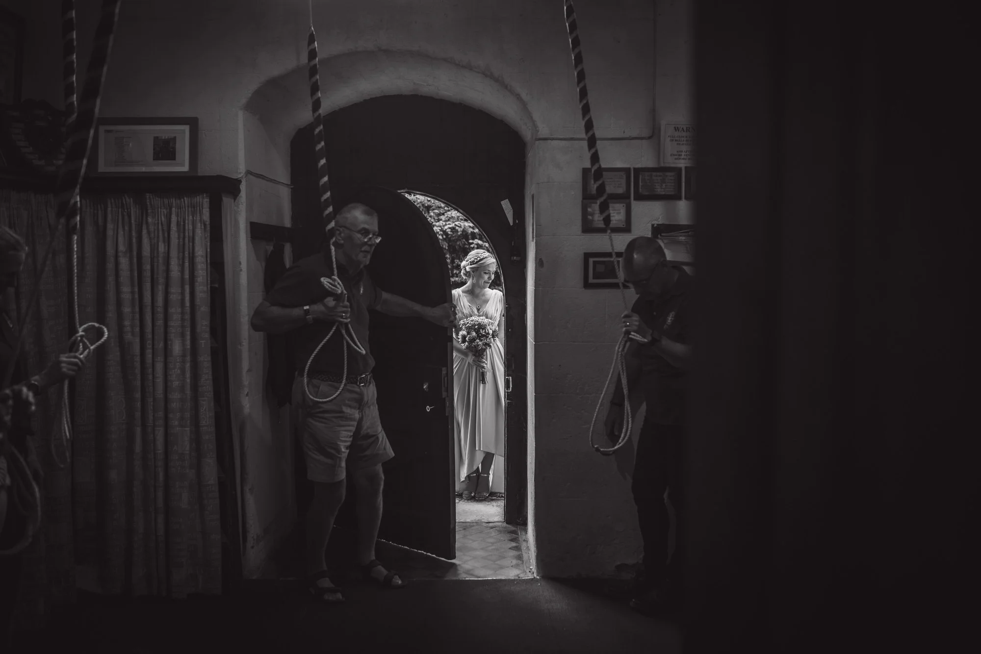 churchbell-ringer-hold-door-for-bridesmaid-Devon-church-wedding.jpg