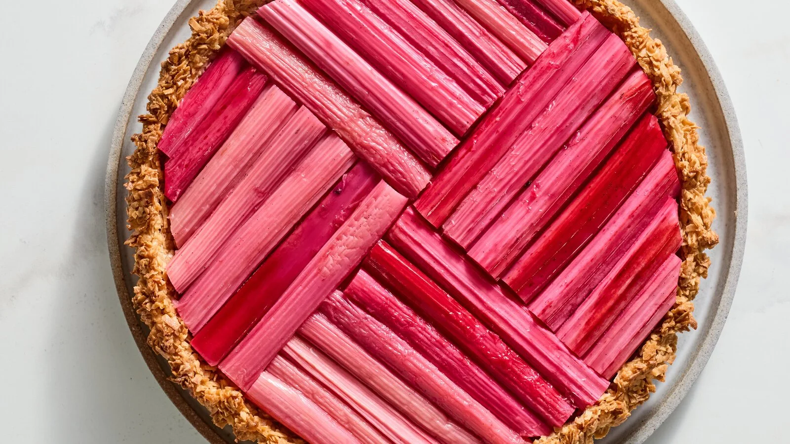 A heart-shaped pink rhubarb tart with a crust covered in chopped nuts.