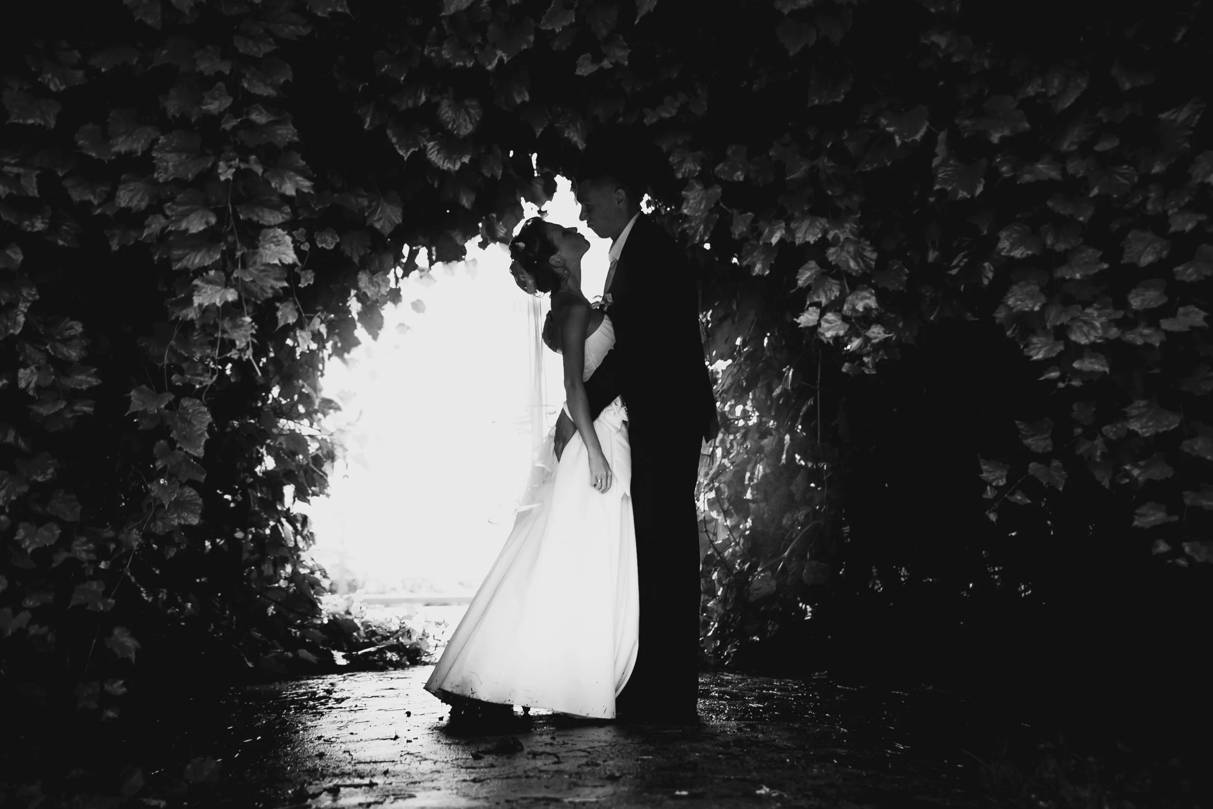Black and white photo of bride and groom dancing at tree tunnel..