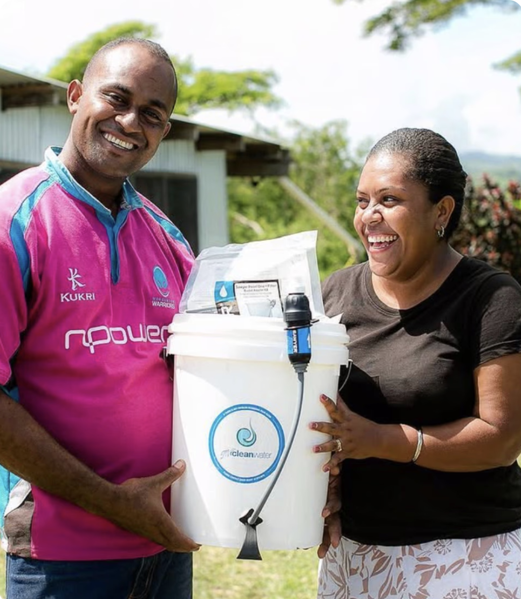 A smiling man and woman holding a water purification device outdoors.