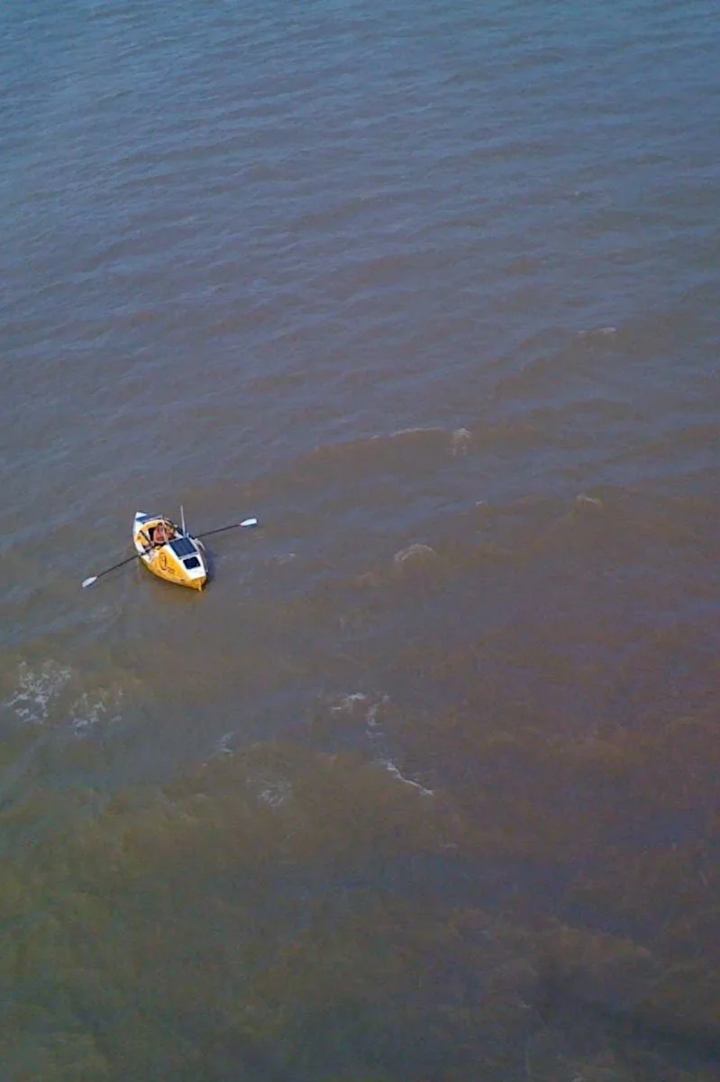 A small yellow boat on a calm body of water, seen from above.