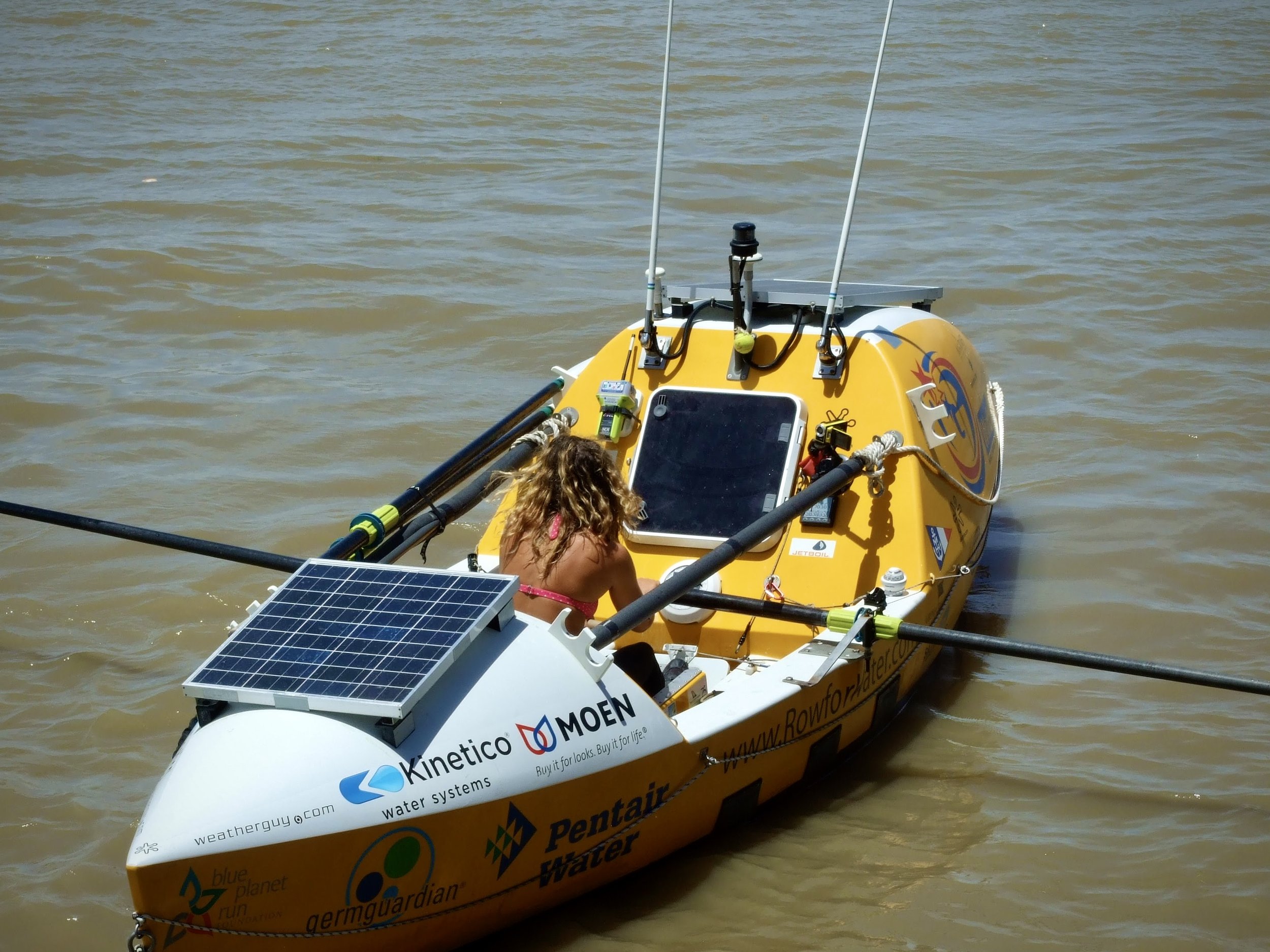 A yellow autonomous boat with solar panels and various equipment on board, floating on water, with a person partially visible in the foreground.