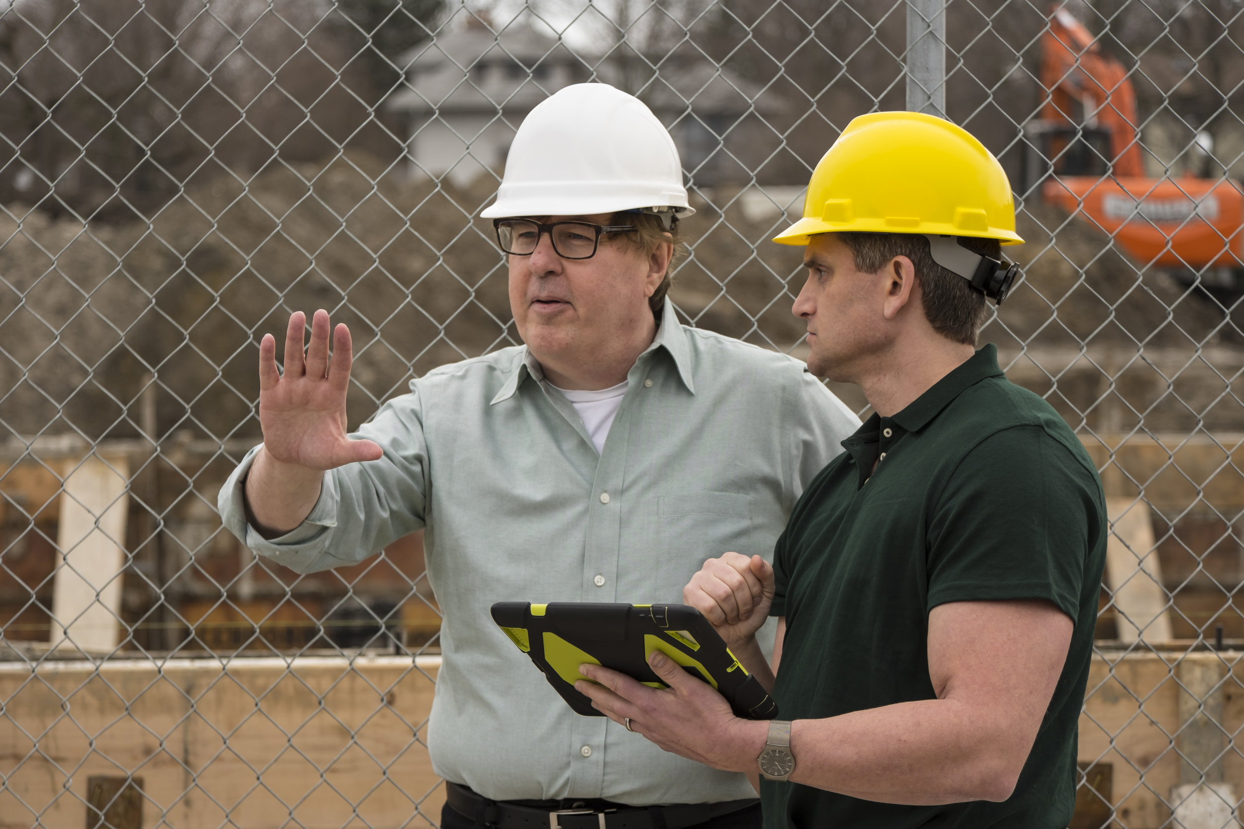 Two workers on a construction site using a tablet