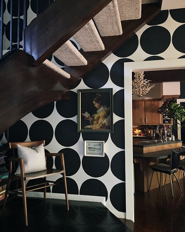 "One of my favorite architectural details in our home; we love this "book nook" under the stairs." says Andrea. "Features: original slate flooring, vintage MCM chair; collected art and circle wall that I painted a few years ago. Peek into our original 1964 kitchen that I love and hate at times, but Reno for that will come later 🖤"