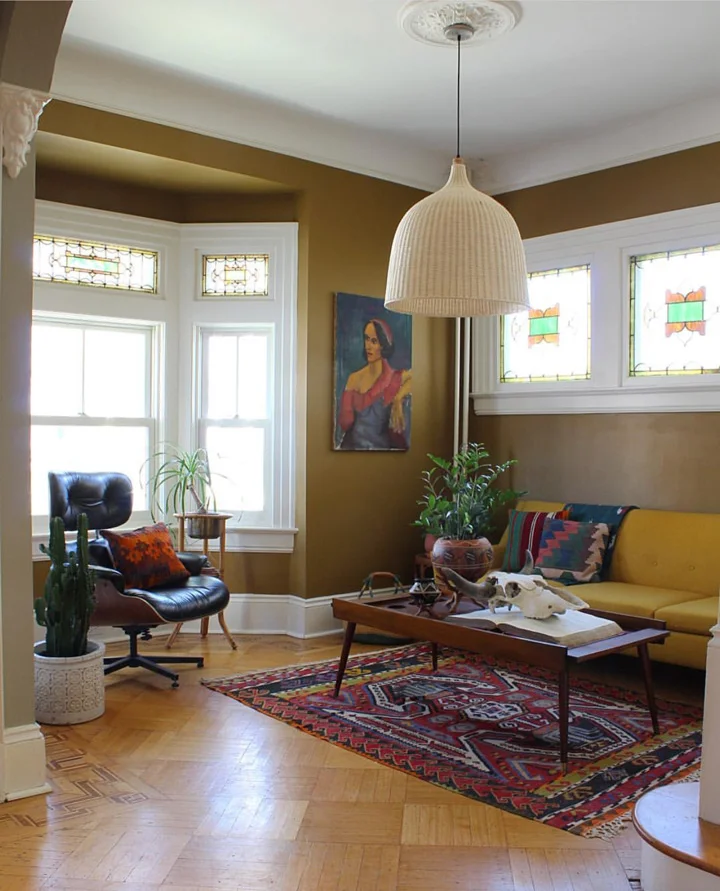 An Eames lounge chair, mustard sofa, stained glass windows and parquet flooring, along with plants and vintage finds; layered to perfection