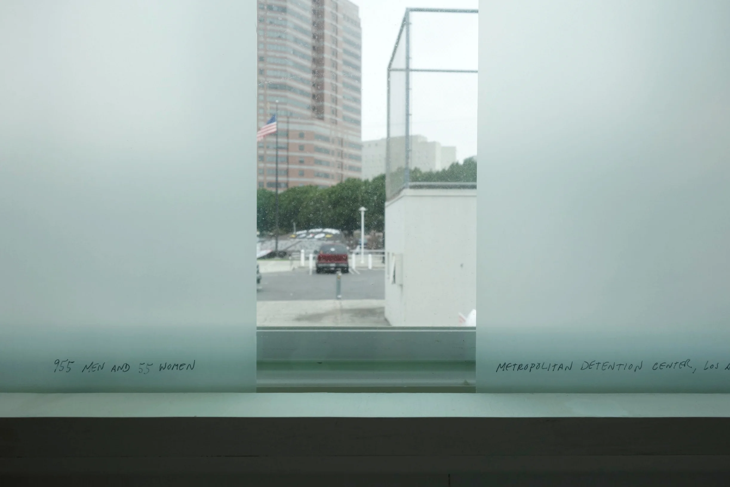 Detail: Ashley Hunt, 955 Men and 55 Women, Metropolitan Detention Center, Los Angeles , 2014. Acetate on glass framing a view of the nearby Metropolitan Detention Center.