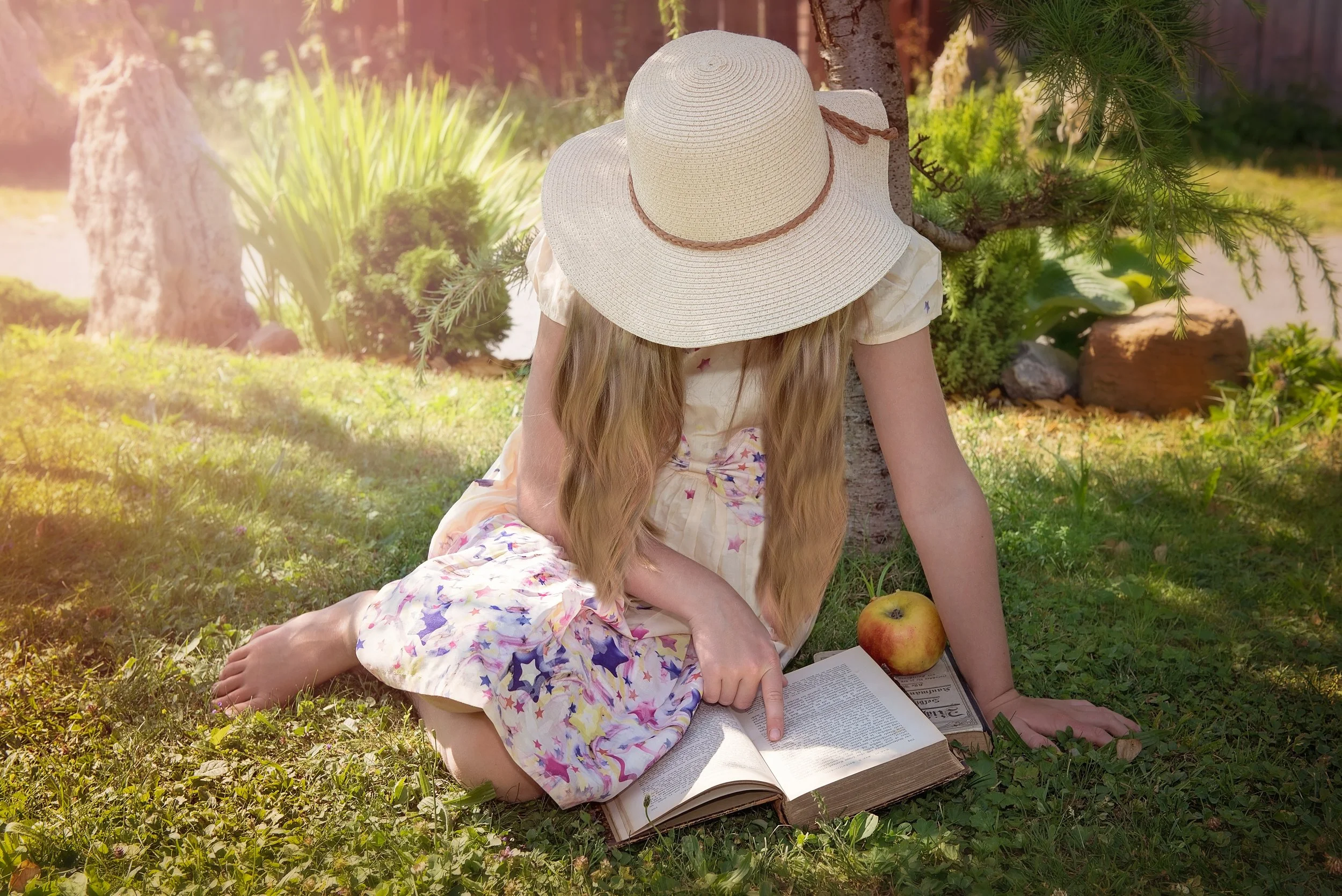 Young Girl in a Sun Hat Reading a Book in a Park