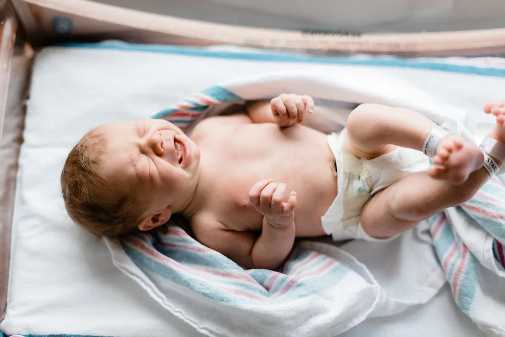 newborn baby crying in hospital bassinet and blanket