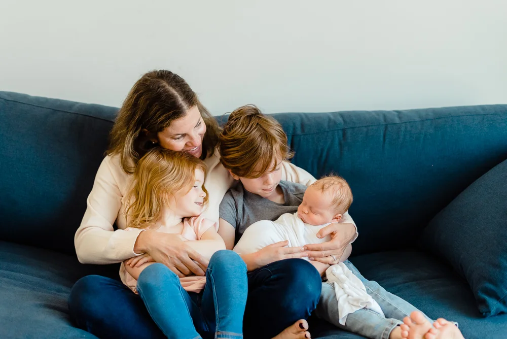 mom, brother and sister sitting on couch holding newborn baby