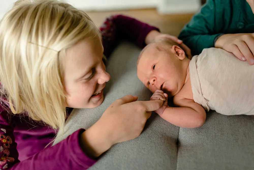 big sister snuggling next to newborn baby sister