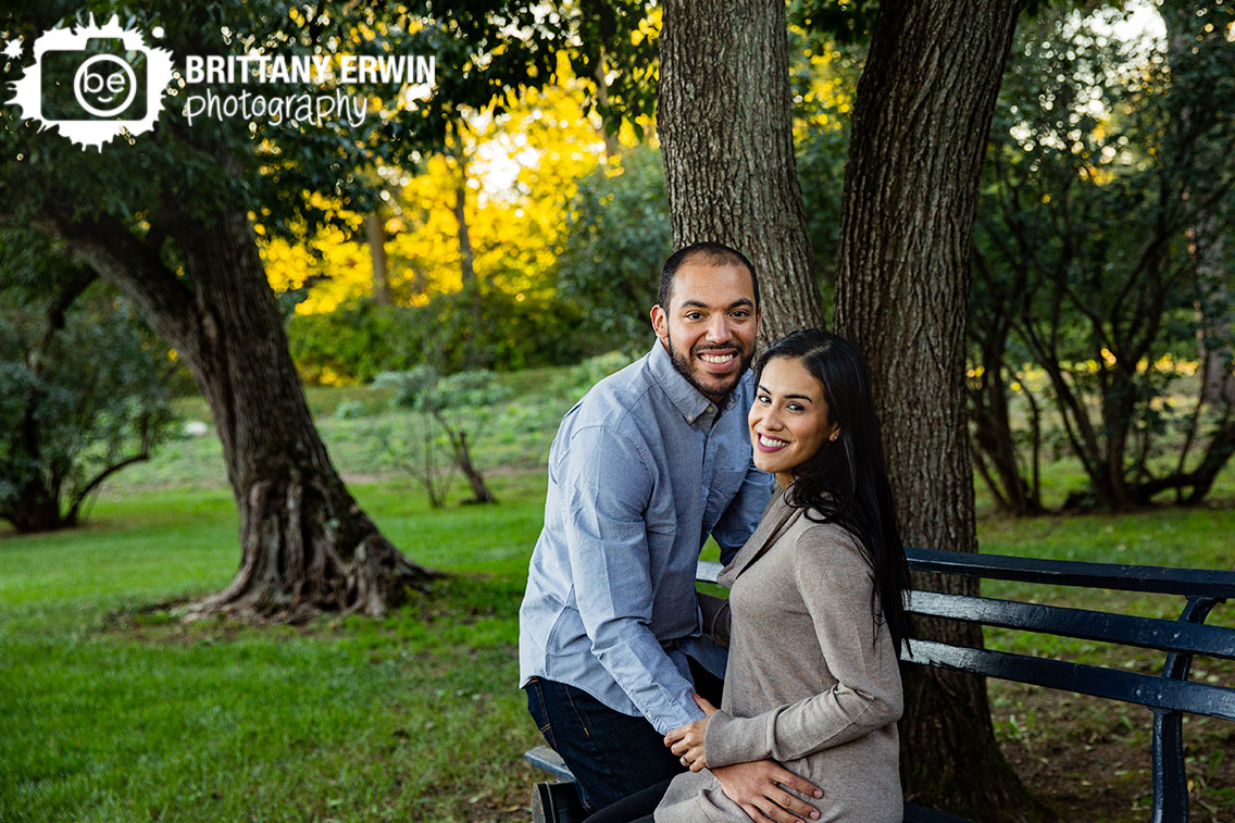 Indianapolis-fall-engagement-portrait-photographer-couple-on-bench-under-trees-holcomb-gardens.jpg