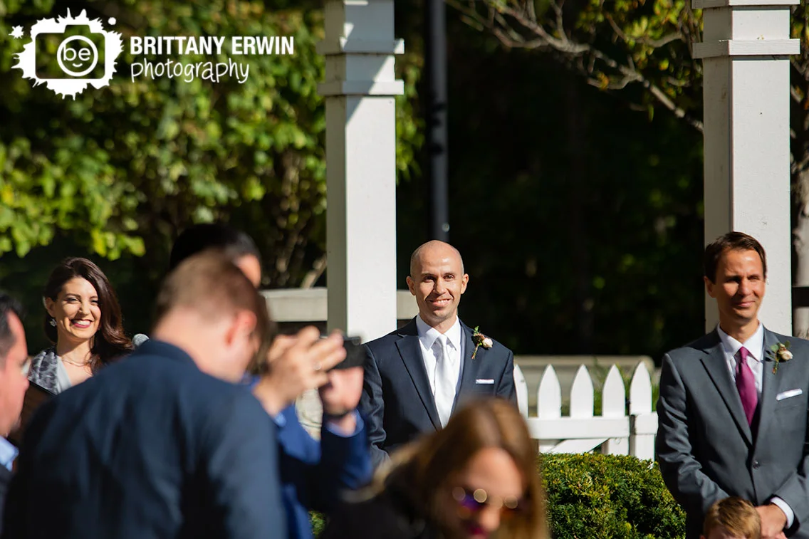 Groom-watching-bride-walk-down-aisle-at-pergola-Historic-Ambassador-House.jpg