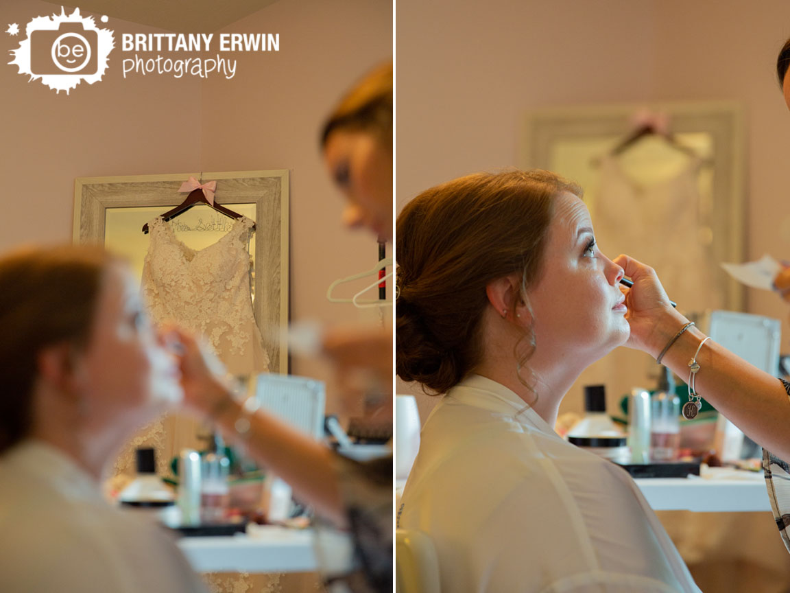 dress-hanging-from-mirror-behind-bride-having-makeup-done.jpg